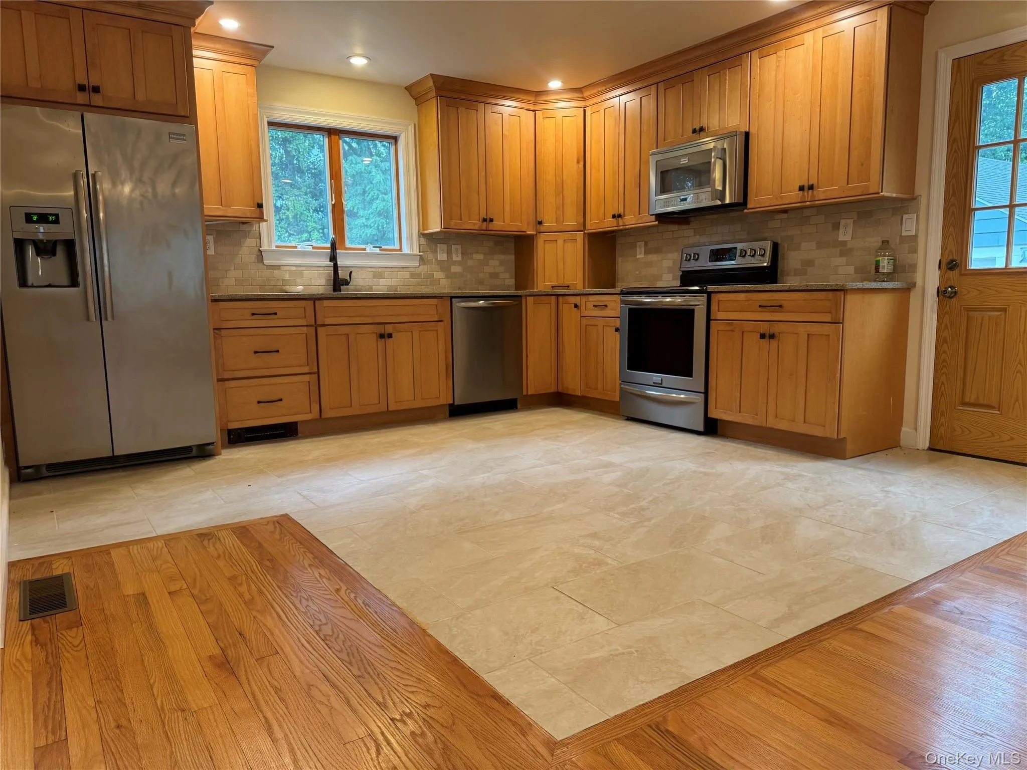 Kitchen featuring stainless steel appliances, decorative backsplash, brown cabinets, recessed lighting, and dark stone countertops Kitchen featuring stainless steel appliances, decorative backsplash, brown cabinets, recessed lighting, and dark stone countertops