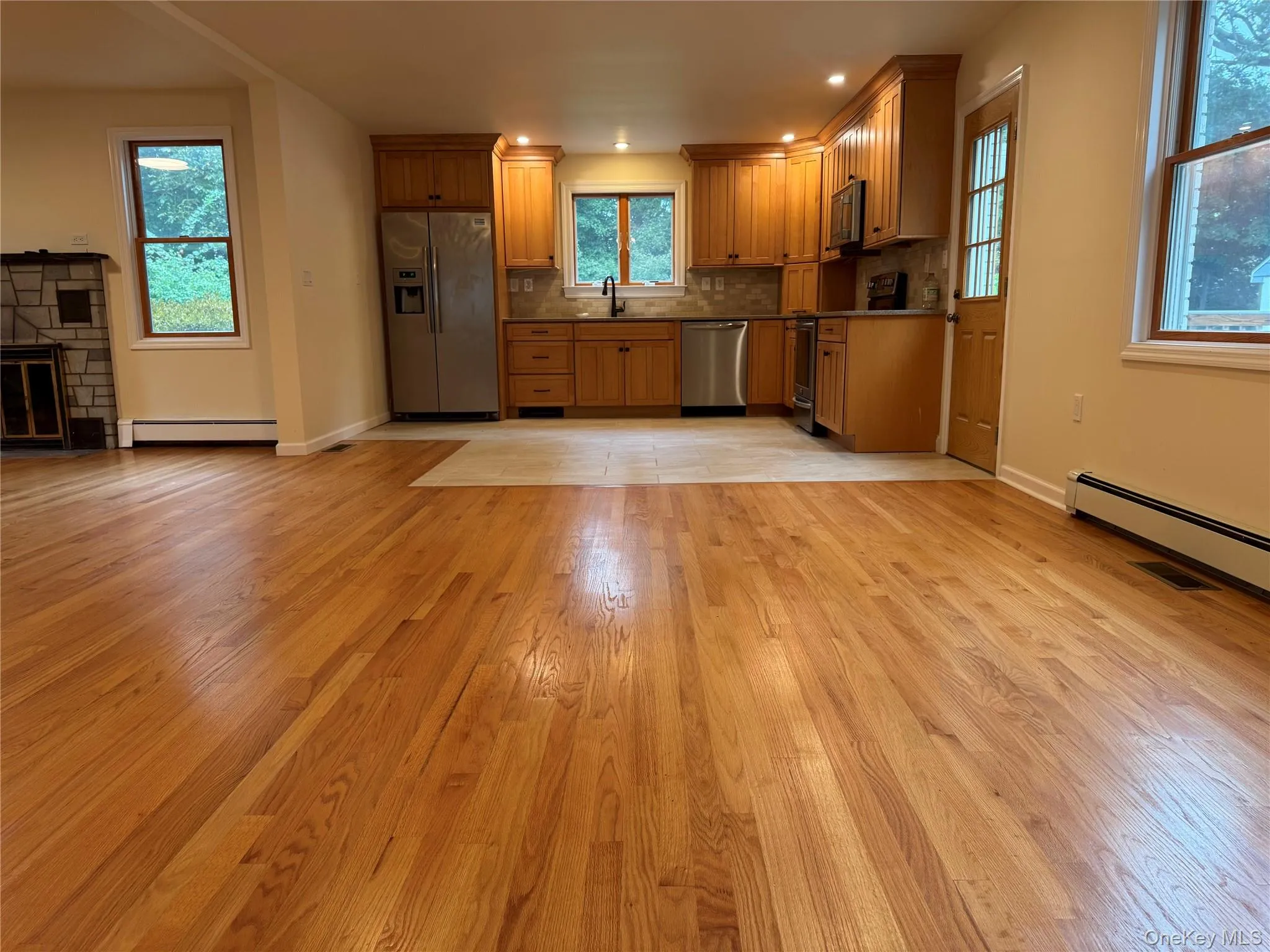 Kitchen featuring brown cabinets, stainless steel appliances, open floor plan, a fireplace, and light wood finished floors Kitchen featuring brown cabinets, stainless steel appliances, open floor plan, a fireplace, and light wood finished floors