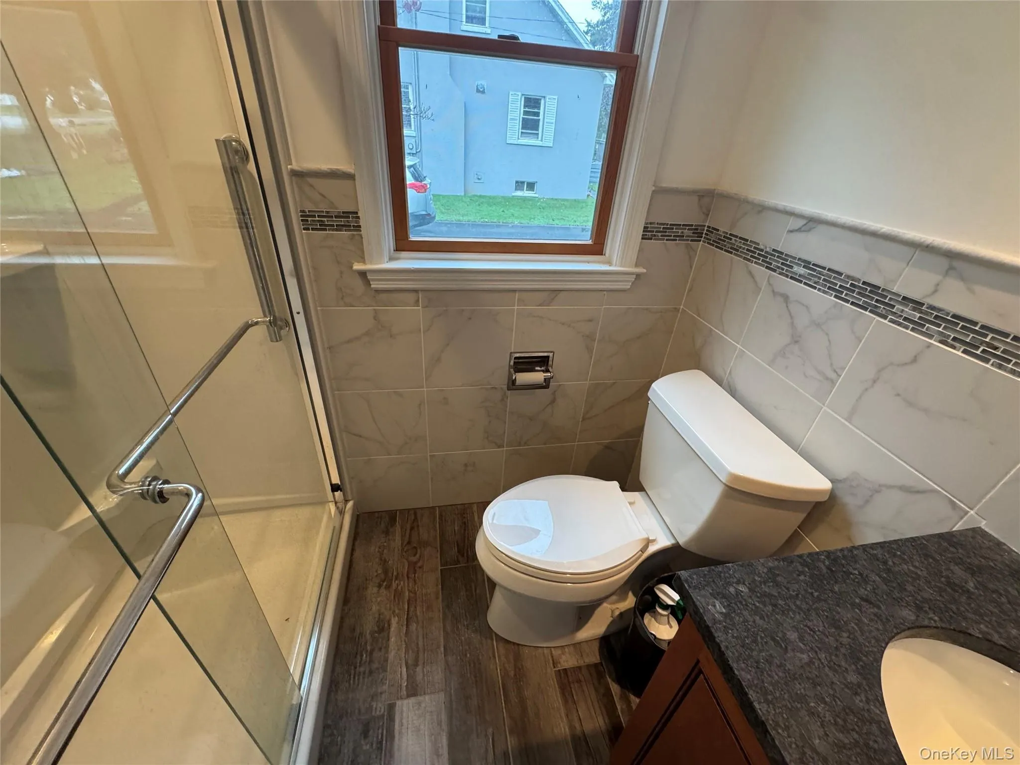 Bathroom featuring vanity, a shower stall, dark wood-style flooring, tile walls, and a wainscoted wall Bathroom featuring vanity, a shower stall, dark wood-style flooring, tile walls, and a wainscoted wall