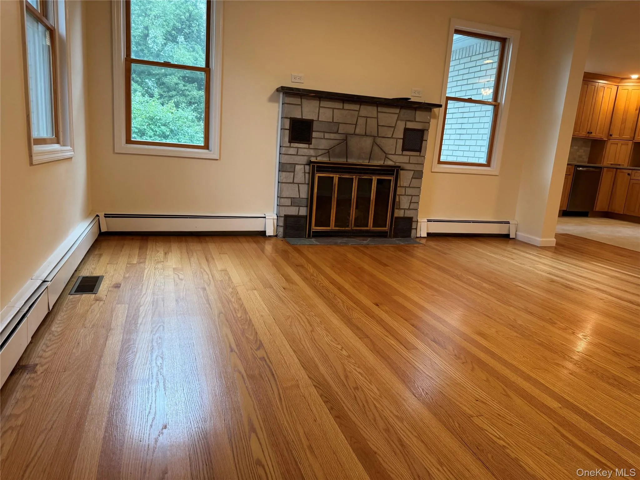 Unfurnished living room with a fireplace, light wood finished floors, and a baseboard heating unit Unfurnished living room with a fireplace, light wood finished floors, and a baseboard heating unit