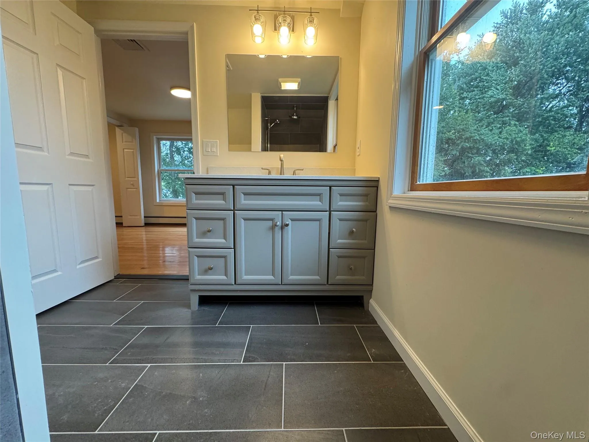 Bathroom featuring vanity, a tile shower, dark tile patterned flooring, and baseboard heating Bathroom featuring vanity, a tile shower, dark tile patterned flooring, and baseboard heating