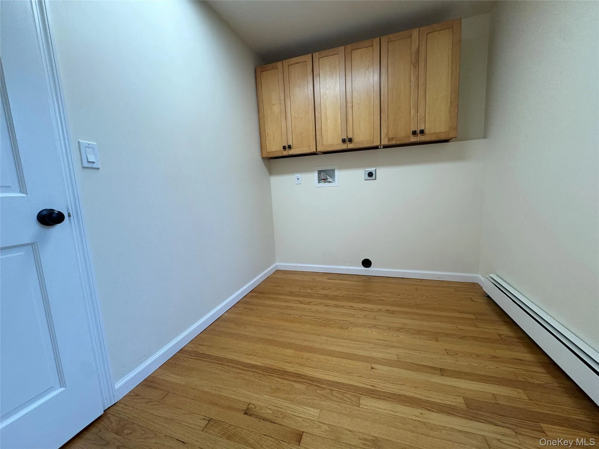 Laundry room with a baseboard heating unit, light wood-type flooring, hookup for a washing machine, cabinet space, and electric dryer hookup Laundry room with a baseboard heating unit, light wood-type flooring, hookup for a washing machine, cabinet space, and electric dryer hookup