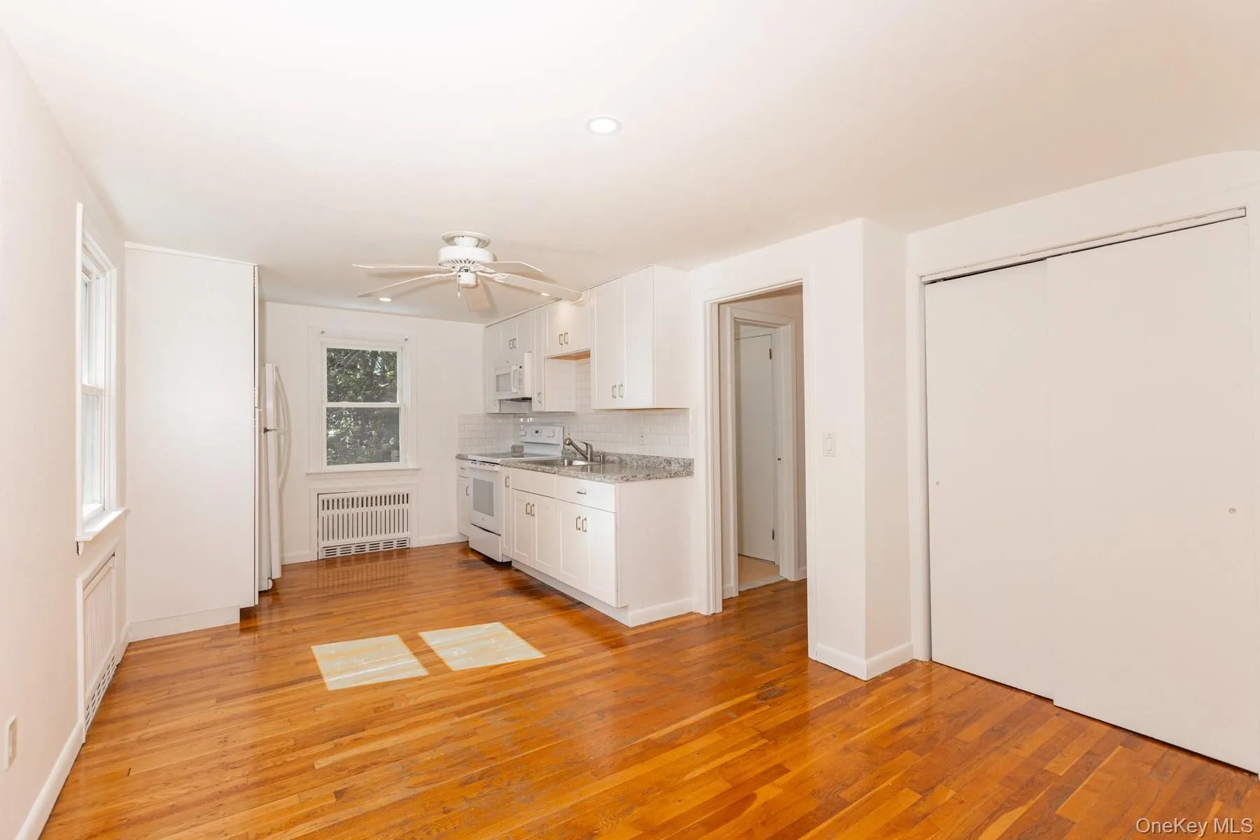 Kitchen featuring white cabinets, white appliances, light countertops, radiator, and light wood-type flooring Kitchen featuring white cabinets, white appliances, light countertops, radiator, and light wood-type flooring