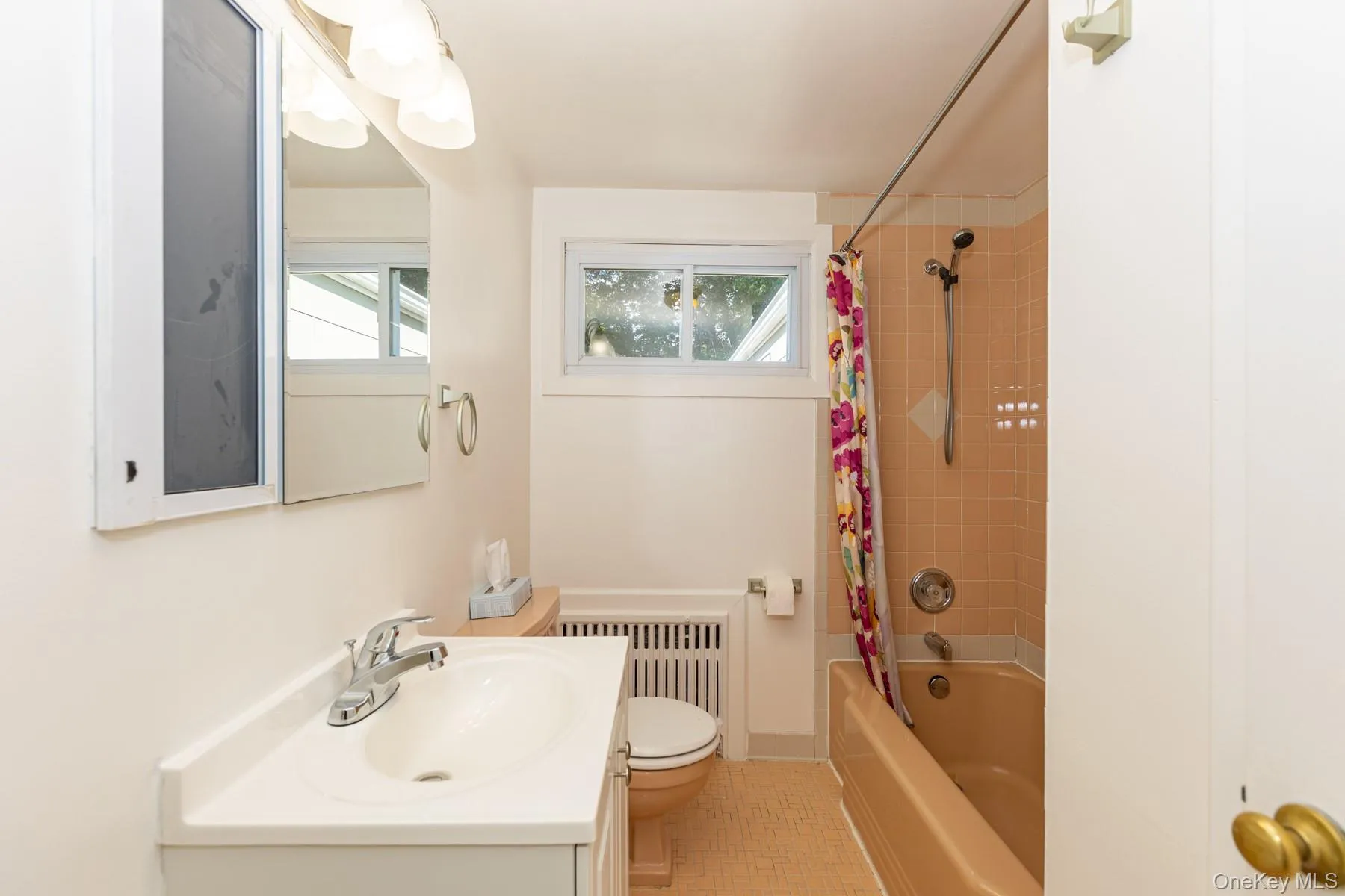 Full bathroom featuring shower / bath combo with shower curtain, vanity, radiator heating unit, and light tile patterned floors Full bathroom featuring shower / bath combo with shower curtain, vanity, radiator heating unit, and light tile patterned floors