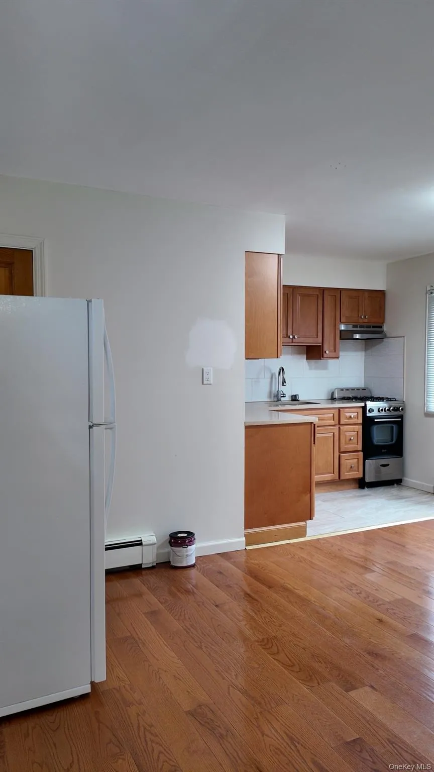 Kitchen featuring brown cabinetry, freestanding refrigerator, light wood-style flooring, range with gas cooktop, and backsplash Kitchen featuring brown cabinetry, freestanding refrigerator, light wood-style flooring, range with gas cooktop, and backsplash