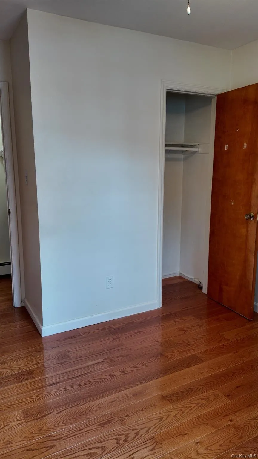 Unfurnished bedroom with wood finished floors, a closet, and baseboard heating Unfurnished bedroom with wood finished floors, a closet, and baseboard heating
