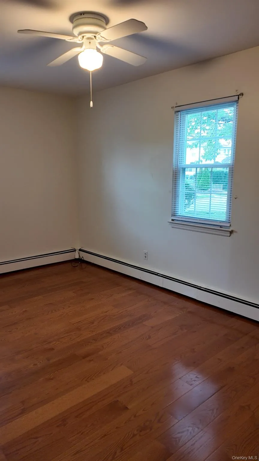 Empty room featuring baseboard heating, dark wood-style flooring, and ceiling fan Empty room featuring baseboard heating, dark wood-style flooring, and ceiling fan