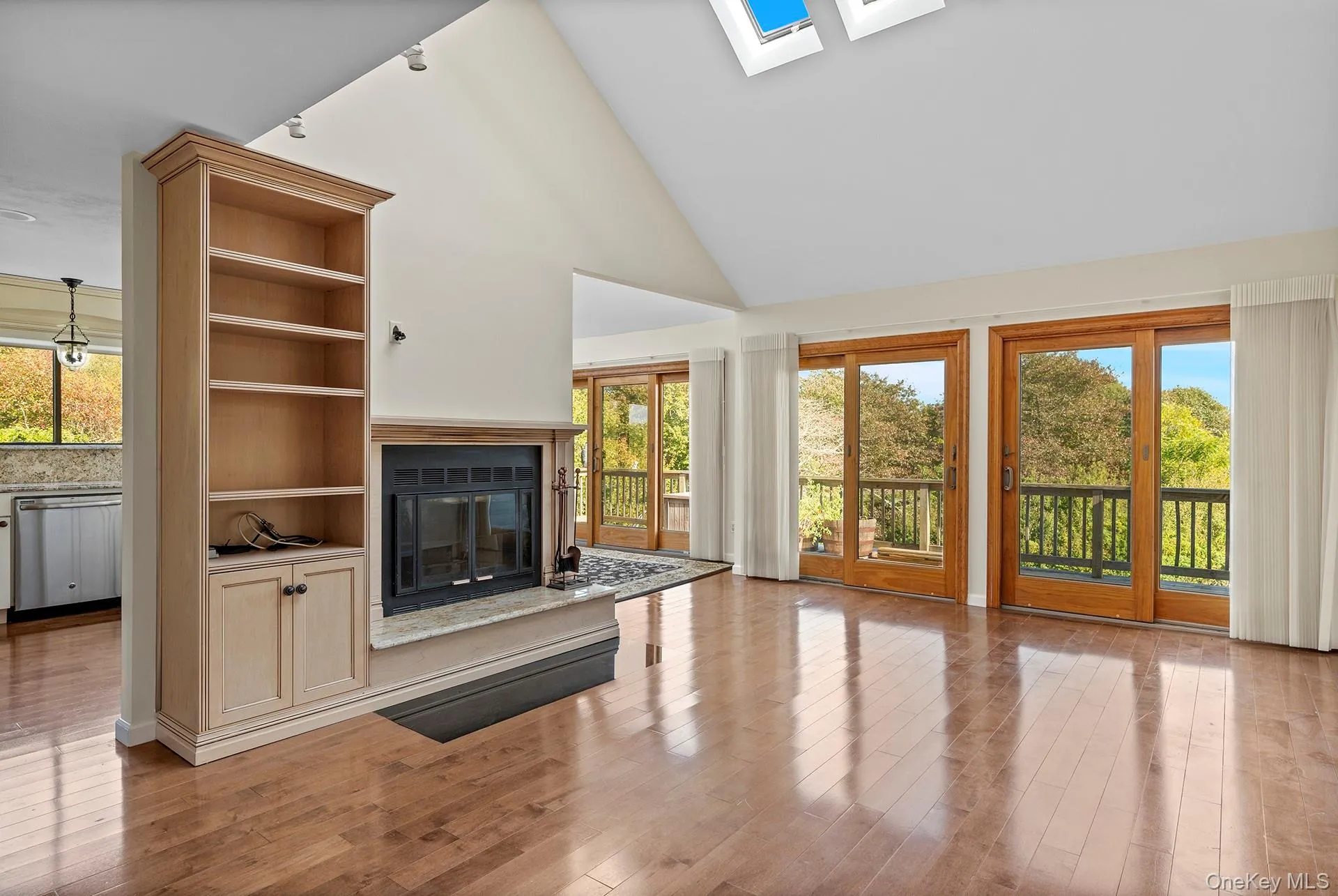 Unfurnished living room with high vaulted ceiling, a skylight, a high end fireplace, and light wood finished floors Unfurnished living room with high vaulted ceiling, a skylight, a high end fireplace, and light wood finished floors