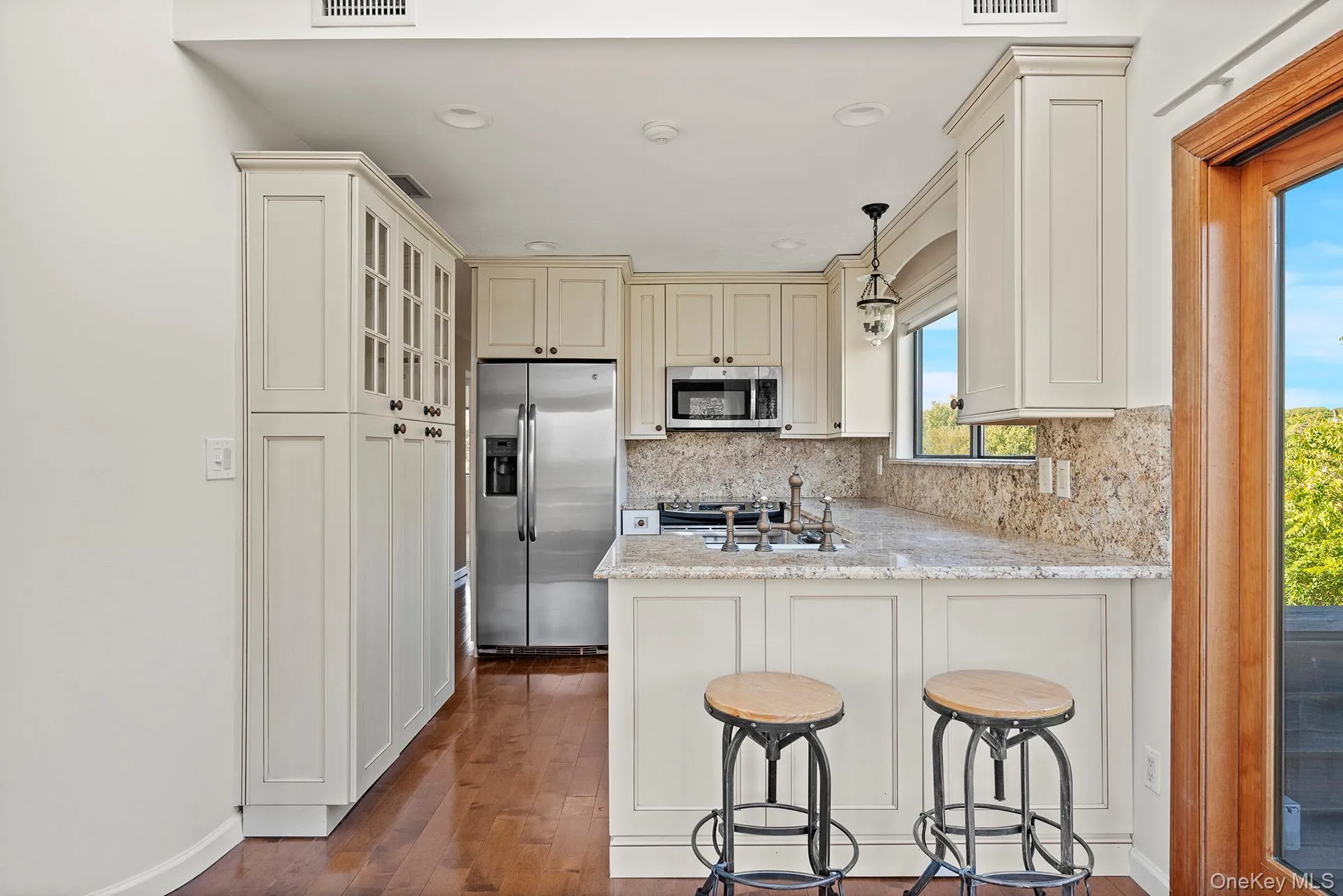 Kitchen with cream cabinets, decorative light fixtures, appliances with stainless steel finishes, decorative backsplash, and light stone countertops Kitchen with cream cabinets, decorative light fixtures, appliances with stainless steel finishes, decorative backsplash, and light stone countertops