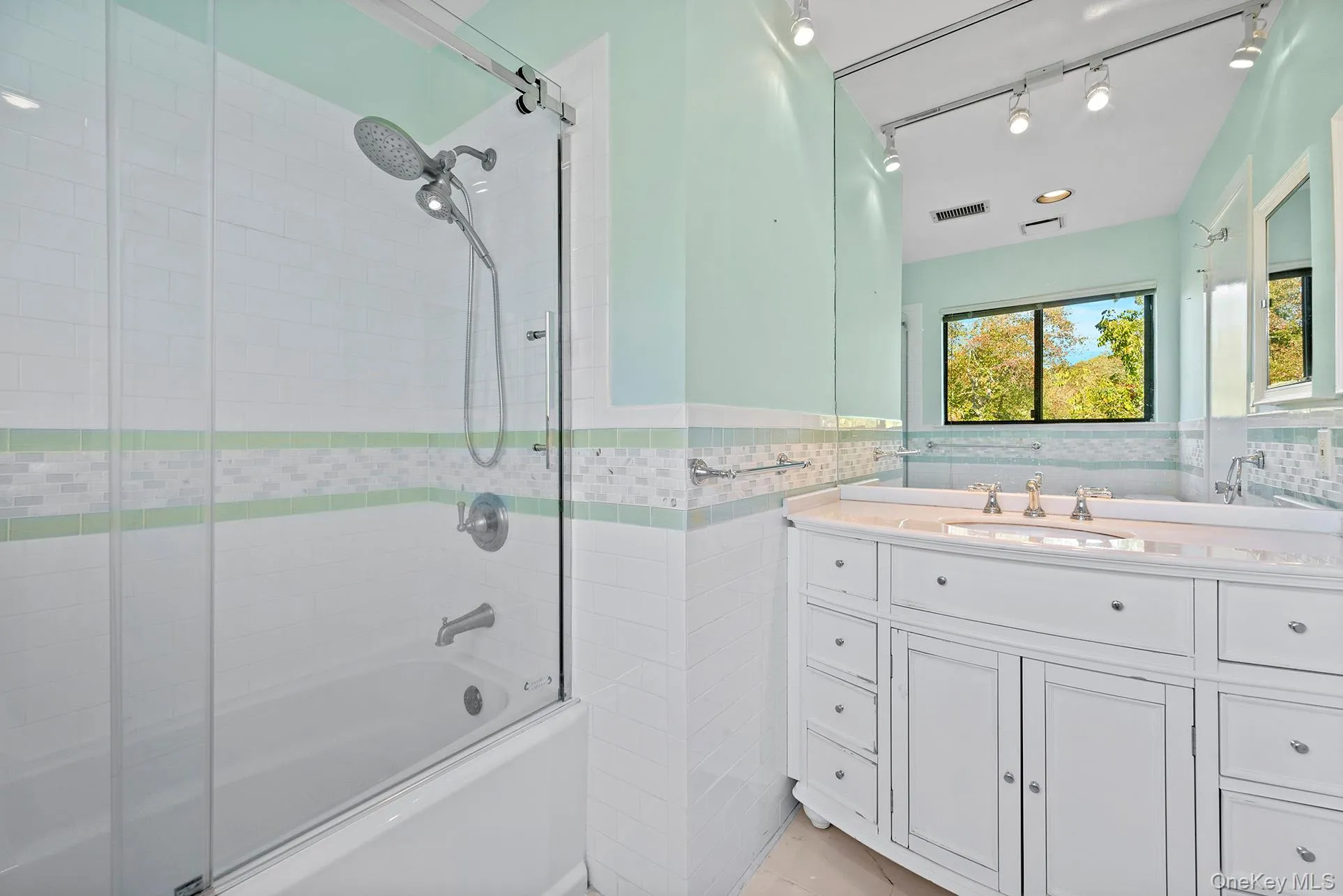 Full bath featuring shower / bath combination with glass door, vanity, tile walls, and a wainscoted wall Full bath featuring shower / bath combination with glass door, vanity, tile walls, and a wainscoted wall