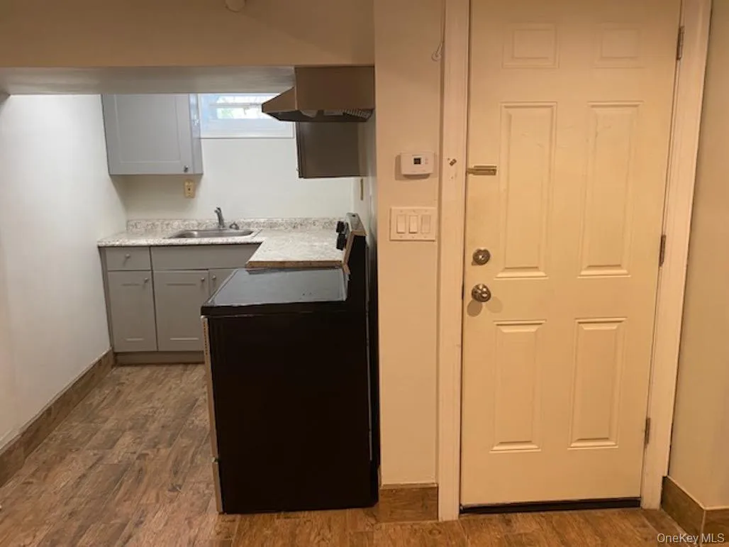 Kitchen with light countertops, ventilation hood, a sink, dark wood finished floors, and gray cabinetry Kitchen with light countertops, ventilation hood, a sink, dark wood finished floors, and gray cabinetry