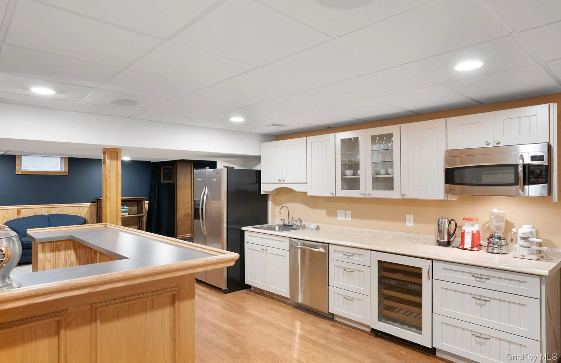 Kitchen with glass insert cabinets, beverage cooler, appliances with stainless steel finishes, a paneled ceiling, and light wood-style floors Kitchen with glass insert cabinets, beverage cooler, appliances with stainless steel finishes, a paneled ceiling, and light wood-style floors