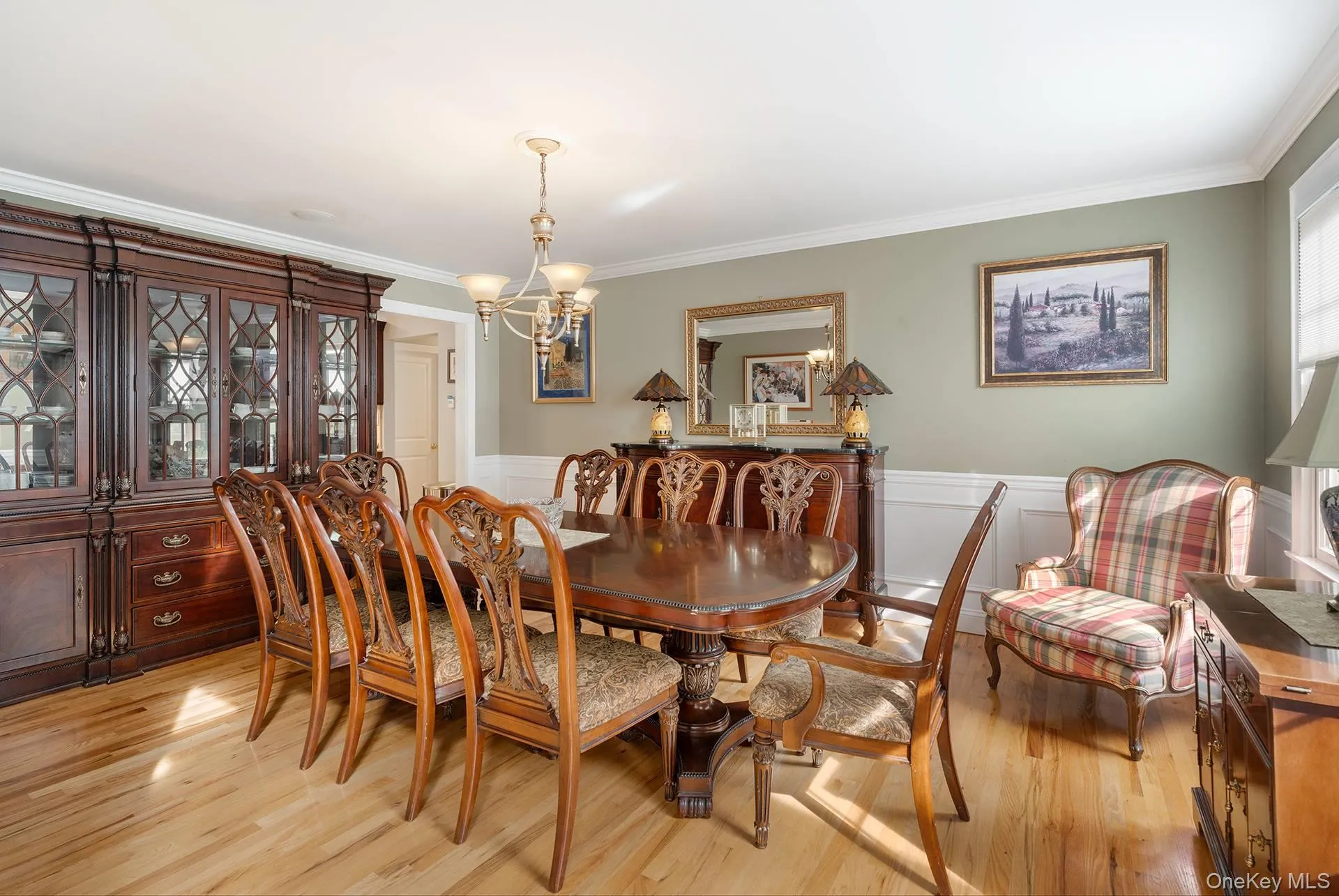 Dining area featuring a chandelier, ornamental molding, light wood-style floors, wainscoting, and a decorative wall Dining area featuring a chandelier, ornamental molding, light wood-style floors, wainscoting, and a decorative wall