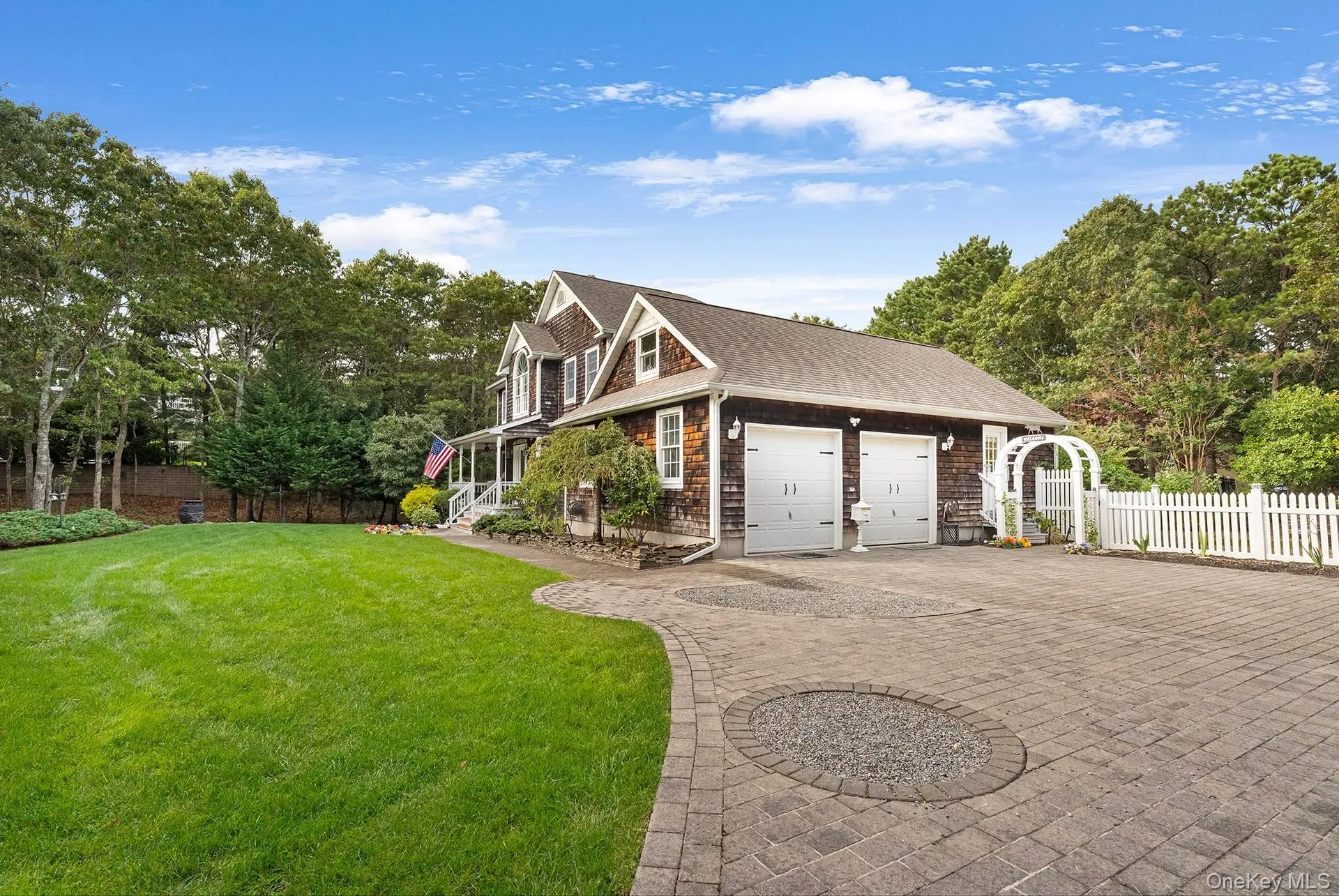 View of side of property with decorative driveway, view of scattered trees, a shingled roof, and a garage View of side of property with decorative driveway, view of scattered trees, a shingled roof, and a garage