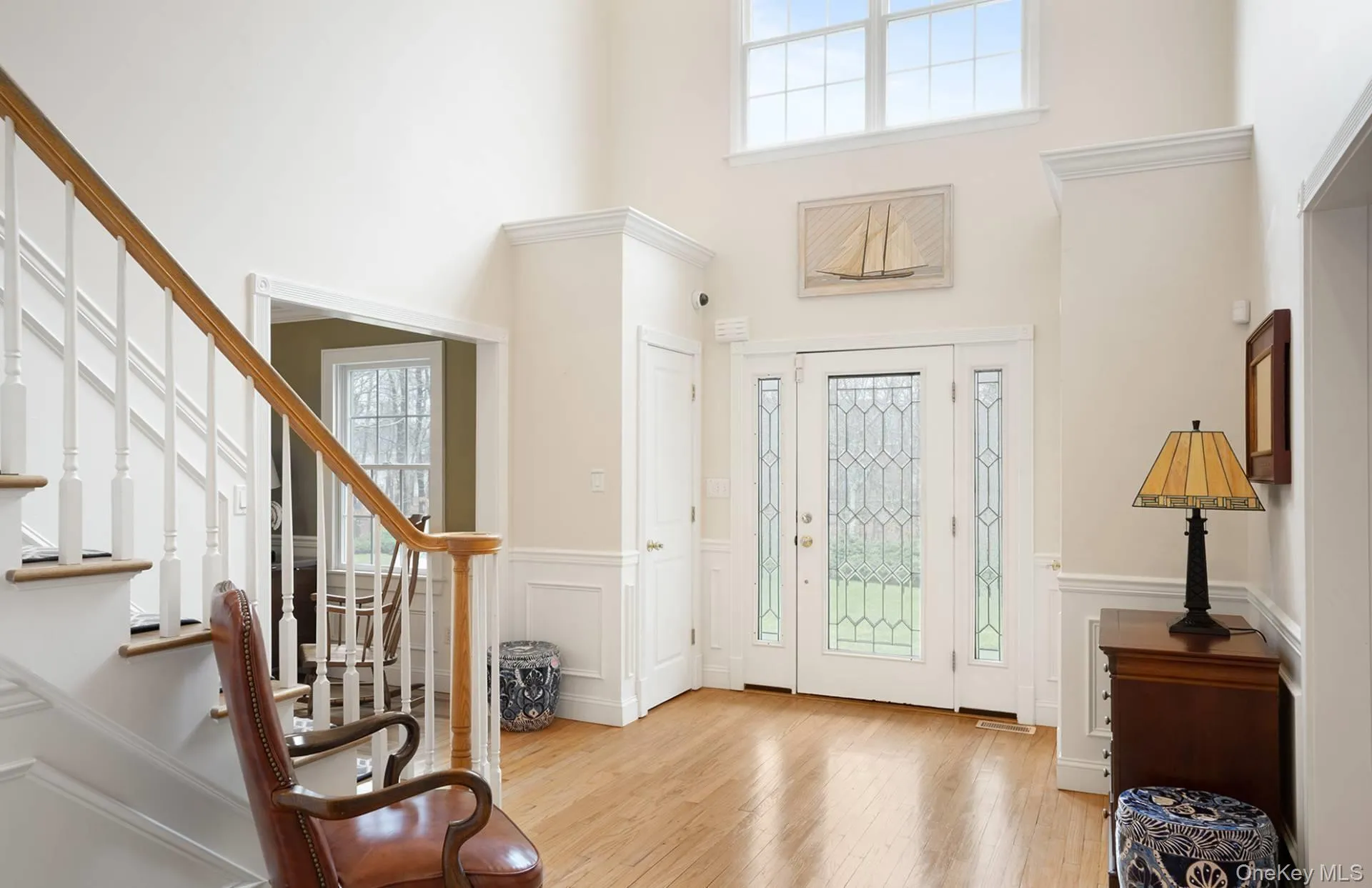Entryway featuring plenty of natural light, light wood-style flooring, wainscoting, a decorative wall, and stairs Entryway featuring plenty of natural light, light wood-style flooring, wainscoting, a decorative wall, and stairs