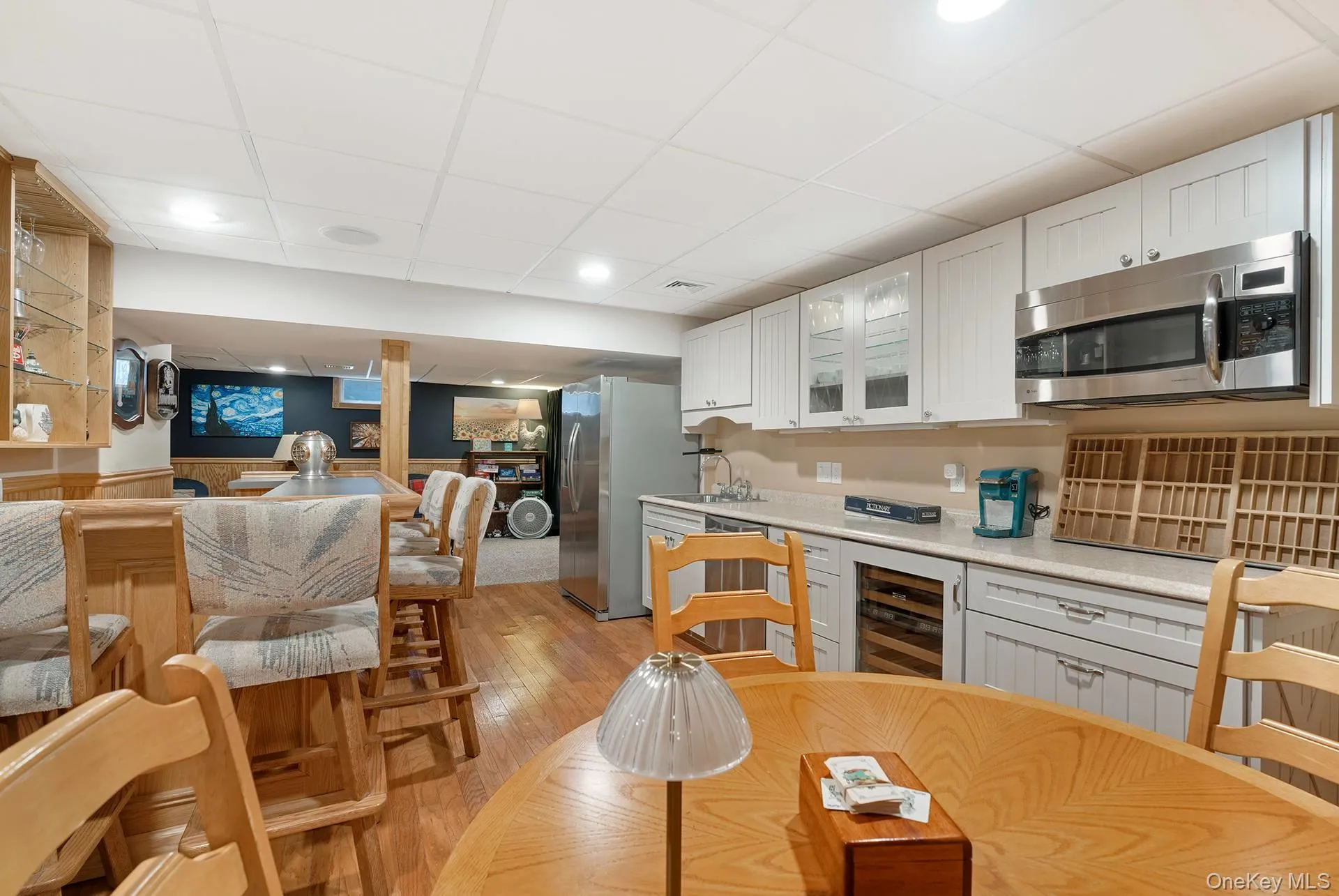 Kitchen featuring white cabinetry, beverage cooler, stainless steel appliances, glass insert cabinets, and light wood-style flooring Kitchen featuring white cabinetry, beverage cooler, stainless steel appliances, glass insert cabinets, and light wood-style flooring