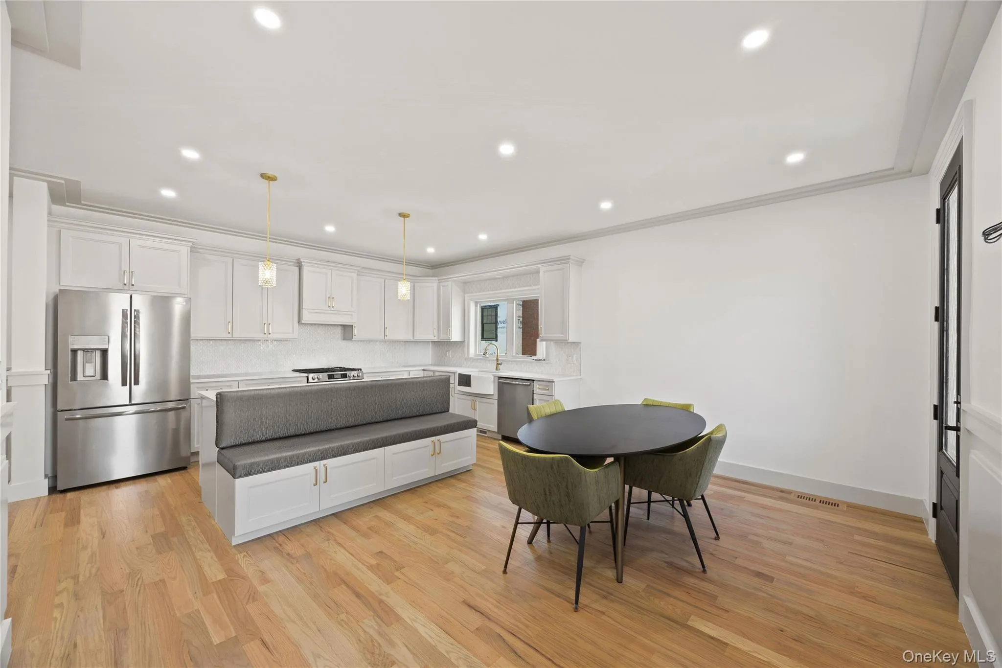 Kitchen featuring stainless steel appliances, light wood-style flooring, white cabinetry, decorative light fixtures, and ornamental molding Kitchen featuring stainless steel appliances, light wood-style flooring, white cabinetry, decorative light fixtures, and ornamental molding