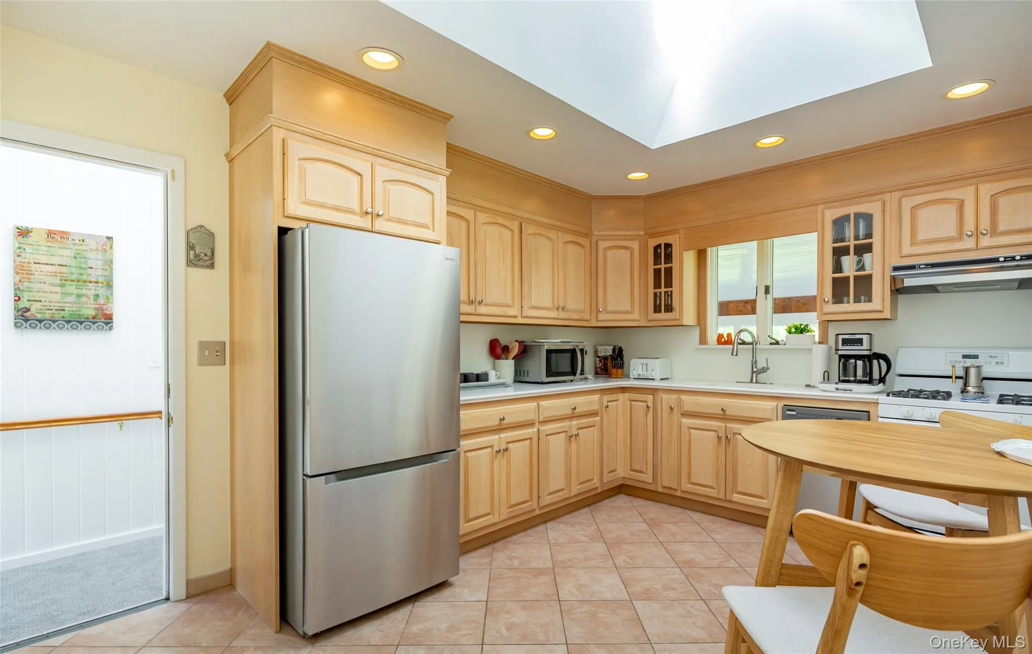 Kitchen featuring recessed lighting, stainless steel appliances, glass insert cabinets, light brown cabinets, and light tile patterned flooring Kitchen featuring recessed lighting, stainless steel appliances, glass insert cabinets, light brown cabinets, and light tile patterned flooring