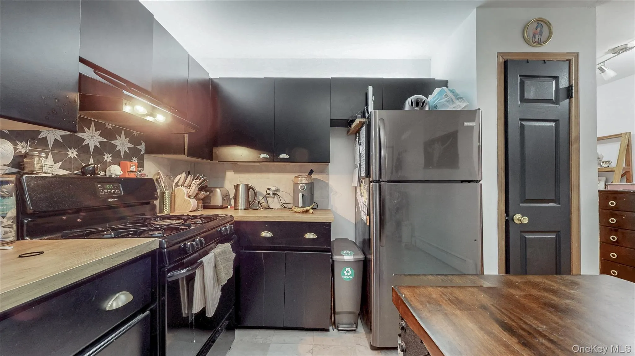 Kitchen featuring black gas stove, freestanding refrigerator, decorative backsplash, wood counters, and dark cabinets Kitchen featuring black gas stove, freestanding refrigerator, decorative backsplash, wood counters, and dark cabinets