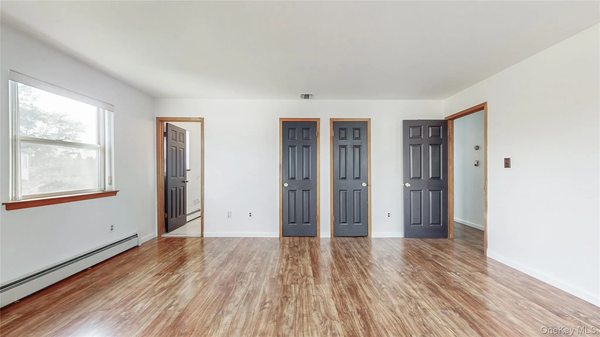 Unfurnished bedroom featuring multiple closets, a baseboard heating unit, light wood-style floors, and ensuite bath Unfurnished bedroom featuring multiple closets, a baseboard heating unit, light wood-style floors, and ensuite bath