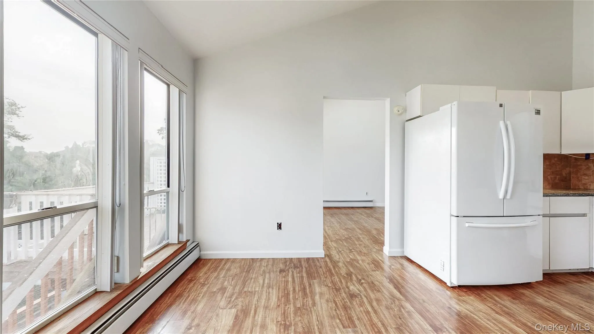 Kitchen featuring freestanding refrigerator, white cabinetry, a baseboard heating unit, vaulted ceiling, and light wood-style flooring Kitchen featuring freestanding refrigerator, white cabinetry, a baseboard heating unit, vaulted ceiling, and light wood-style flooring