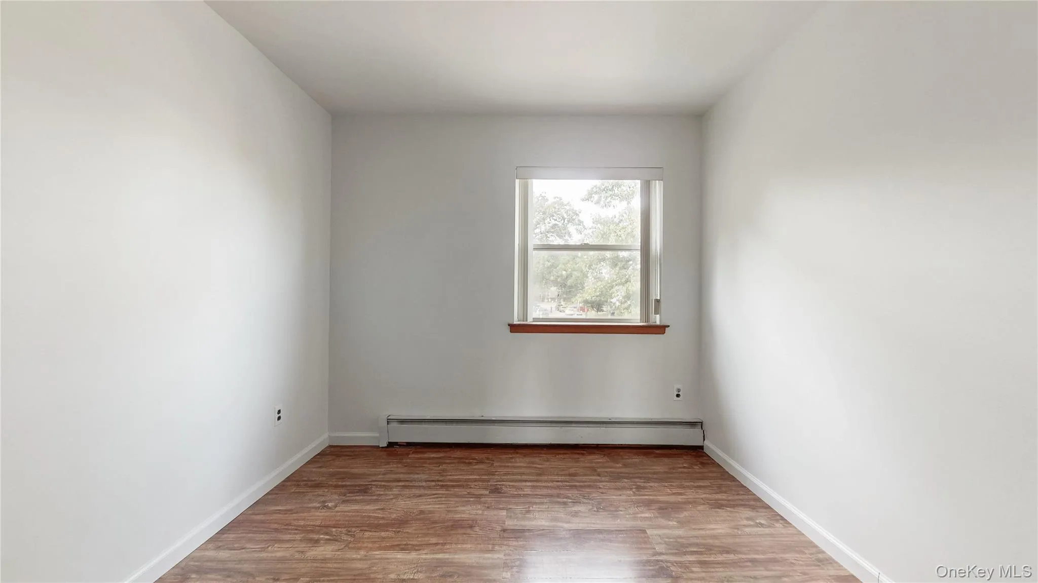 Unfurnished room with wood finished floors and baseboard heating Unfurnished room with wood finished floors and baseboard heating