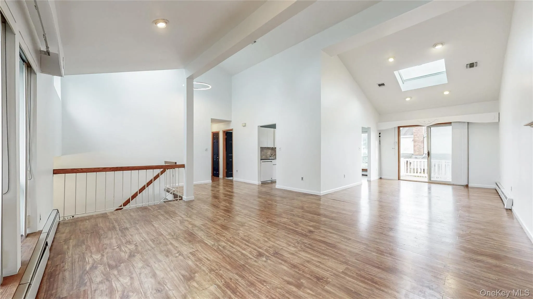 Unfurnished living room featuring high vaulted ceiling, baseboard heating, light wood finished floors, and a skylight Unfurnished living room featuring high vaulted ceiling, baseboard heating, light wood finished floors, and a skylight