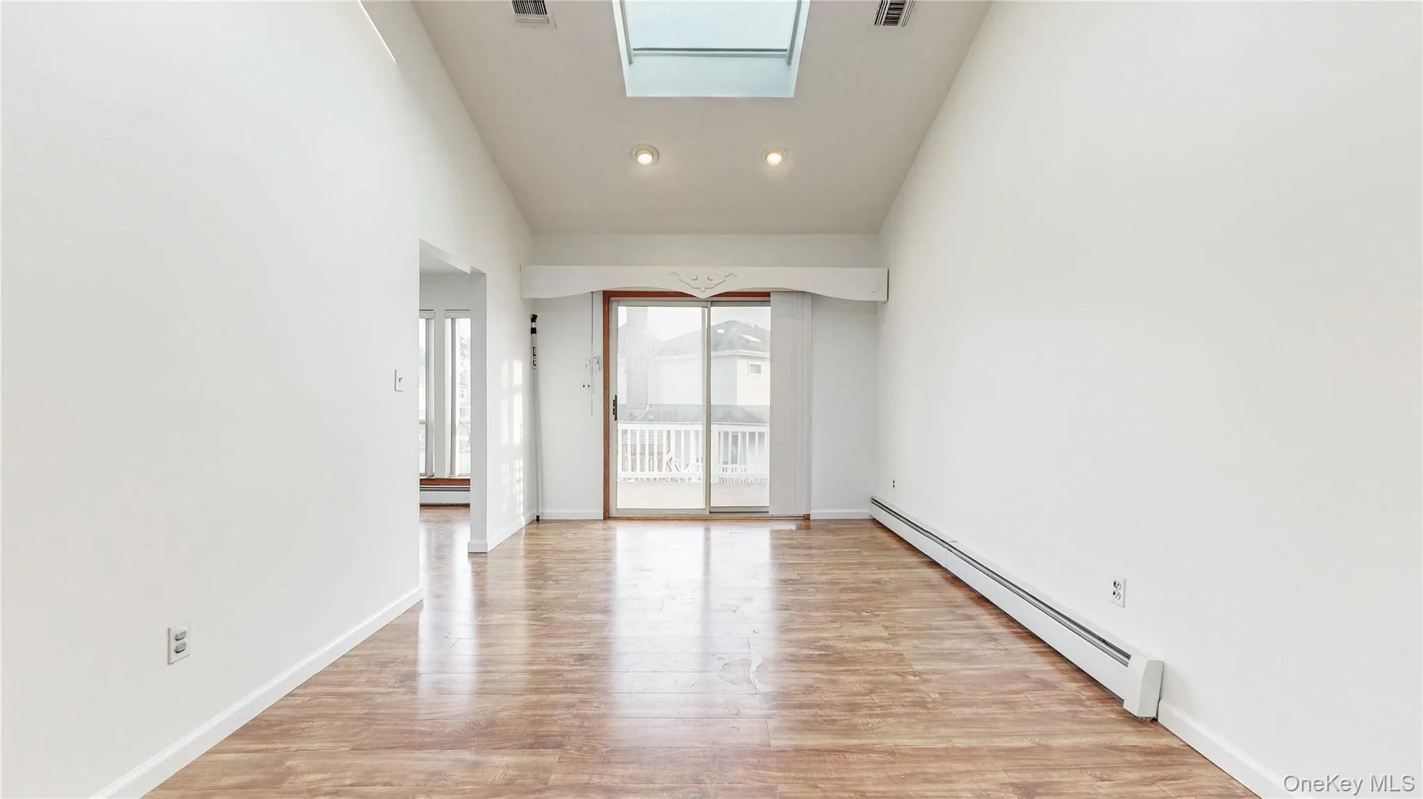 Spare room featuring a baseboard heating unit, a skylight, light wood-style floors, high vaulted ceiling, and recessed lighting Spare room featuring a baseboard heating unit, a skylight, light wood-style floors, high vaulted ceiling, and recessed lighting