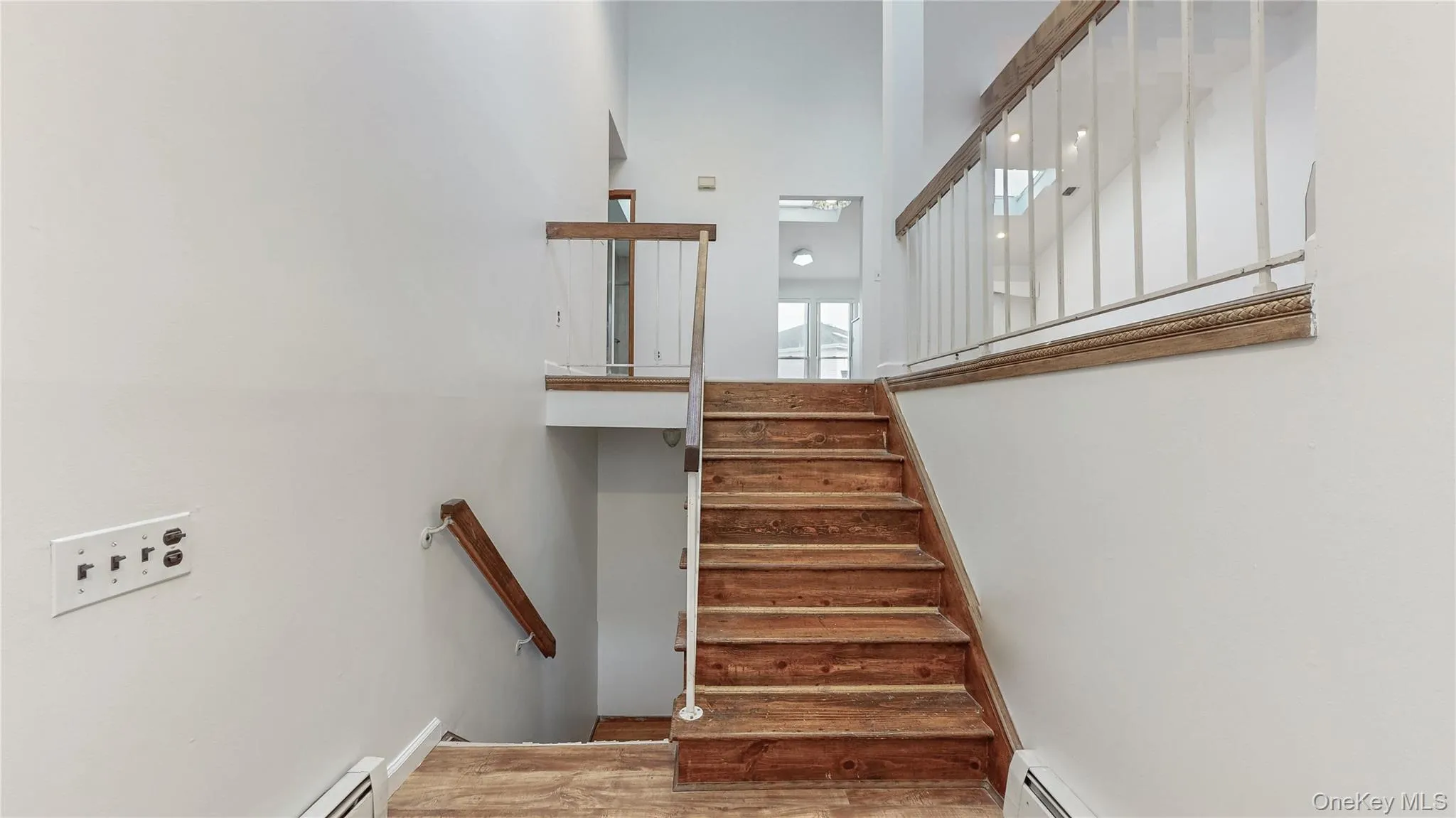 Stairway with a baseboard radiator, wood finished floors, and a towering ceiling Stairway with a baseboard radiator, wood finished floors, and a towering ceiling