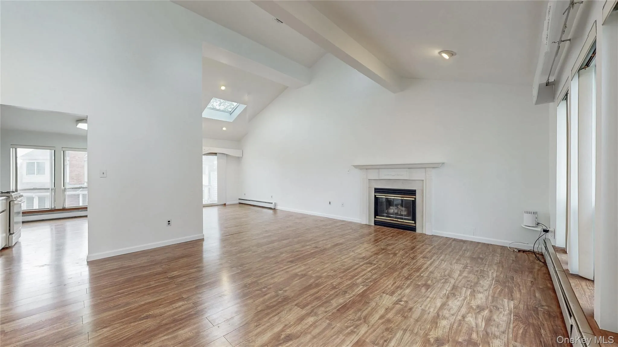 Unfurnished living room with beamed ceiling, a glass covered fireplace, light wood finished floors, high vaulted ceiling, and a baseboard heating unit Unfurnished living room with beamed ceiling, a glass covered fireplace, light wood finished floors, high vaulted ceiling, and a baseboard heating unit