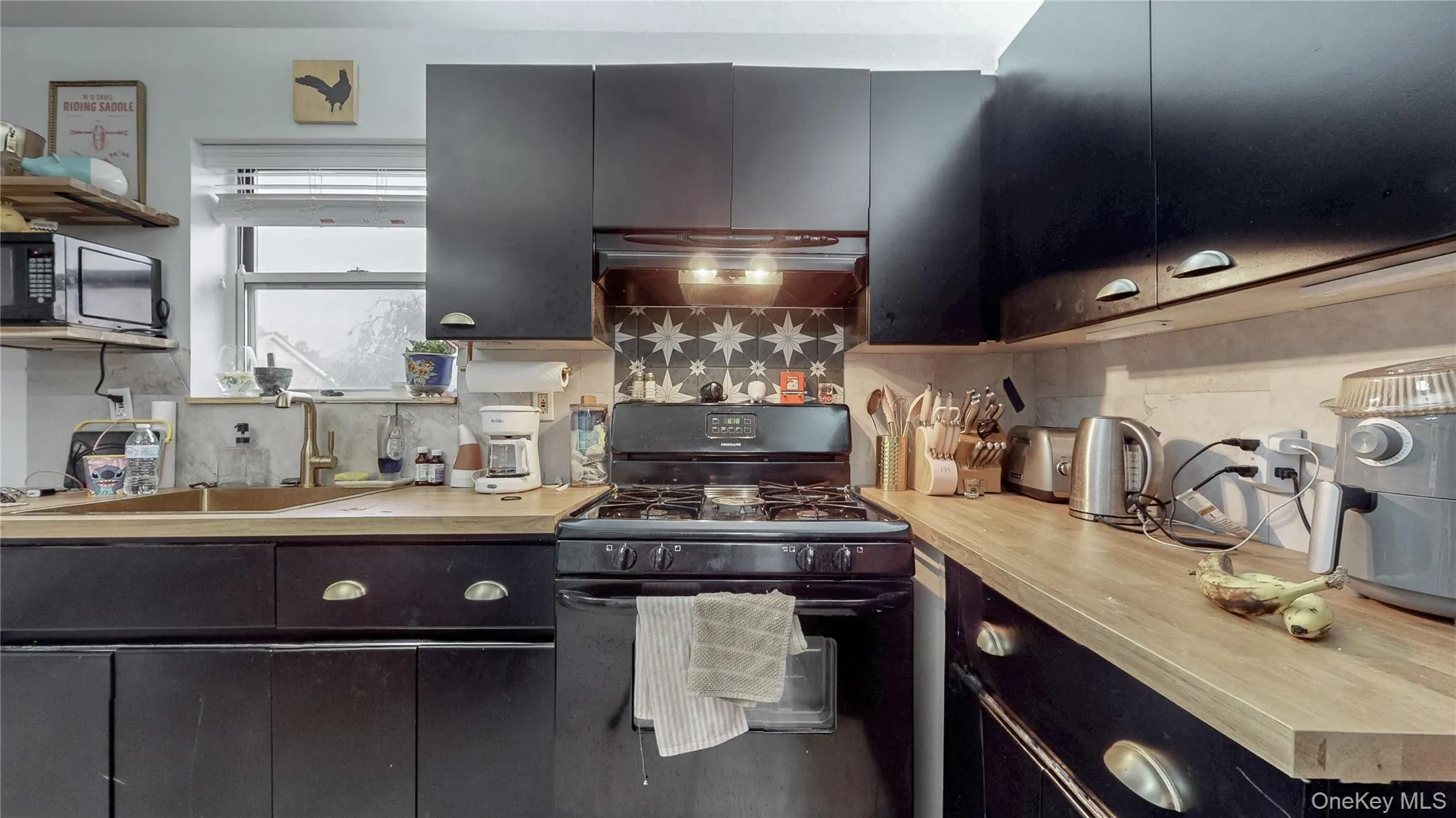 Kitchen with black appliances, backsplash, dark cabinets, wall chimney exhaust hood, and light countertops Kitchen with black appliances, backsplash, dark cabinets, wall chimney exhaust hood, and light countertops