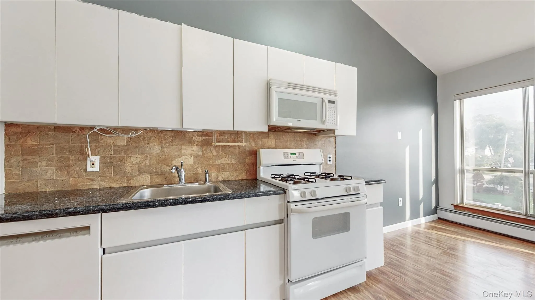 Kitchen with white appliances, tasteful backsplash, white cabinetry, light wood-type flooring, and lofted ceiling Kitchen with white appliances, tasteful backsplash, white cabinetry, light wood-type flooring, and lofted ceiling