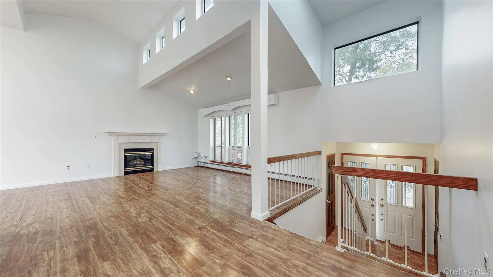 Unfurnished living room featuring high vaulted ceiling, light wood-style flooring, a glass covered fireplace, and a baseboard heating unit Unfurnished living room featuring high vaulted ceiling, light wood-style flooring, a glass covered fireplace, and a baseboard heating unit
