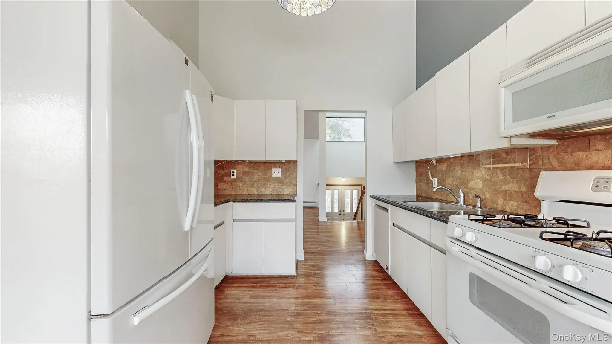 Kitchen featuring white appliances, light wood finished floors, and white cabinetry Kitchen featuring white appliances, light wood finished floors, and white cabinetry