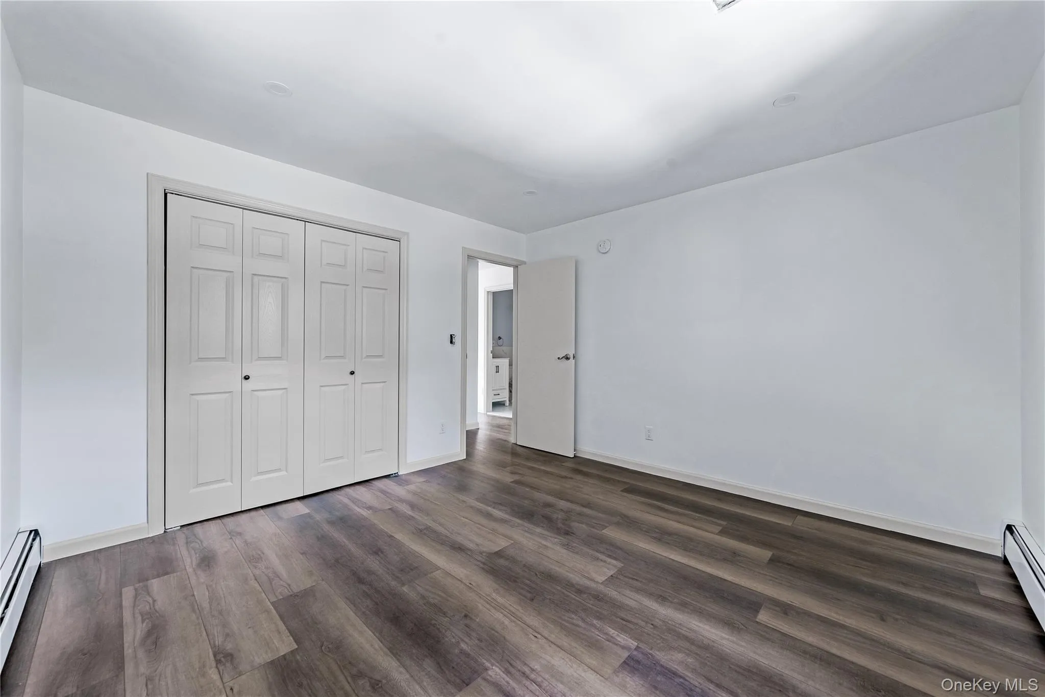 Unfurnished bedroom with dark wood-style flooring, baseboard heating, and a closet Unfurnished bedroom with dark wood-style flooring, baseboard heating, and a closet