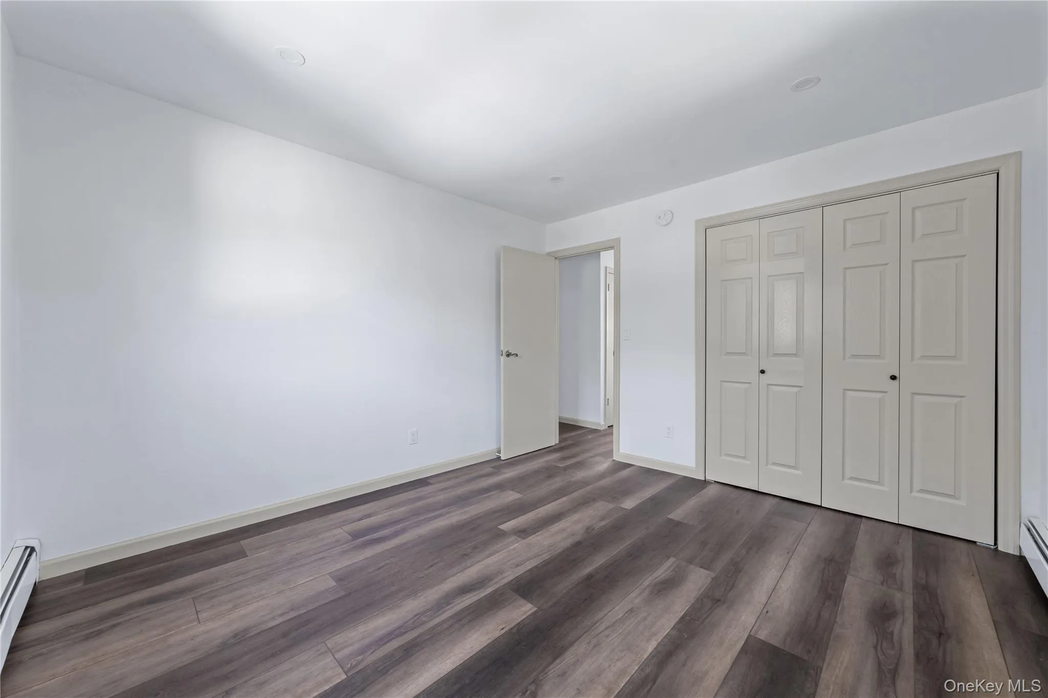 Unfurnished bedroom with dark wood-type flooring, a closet, and a baseboard radiator Unfurnished bedroom with dark wood-type flooring, a closet, and a baseboard radiator