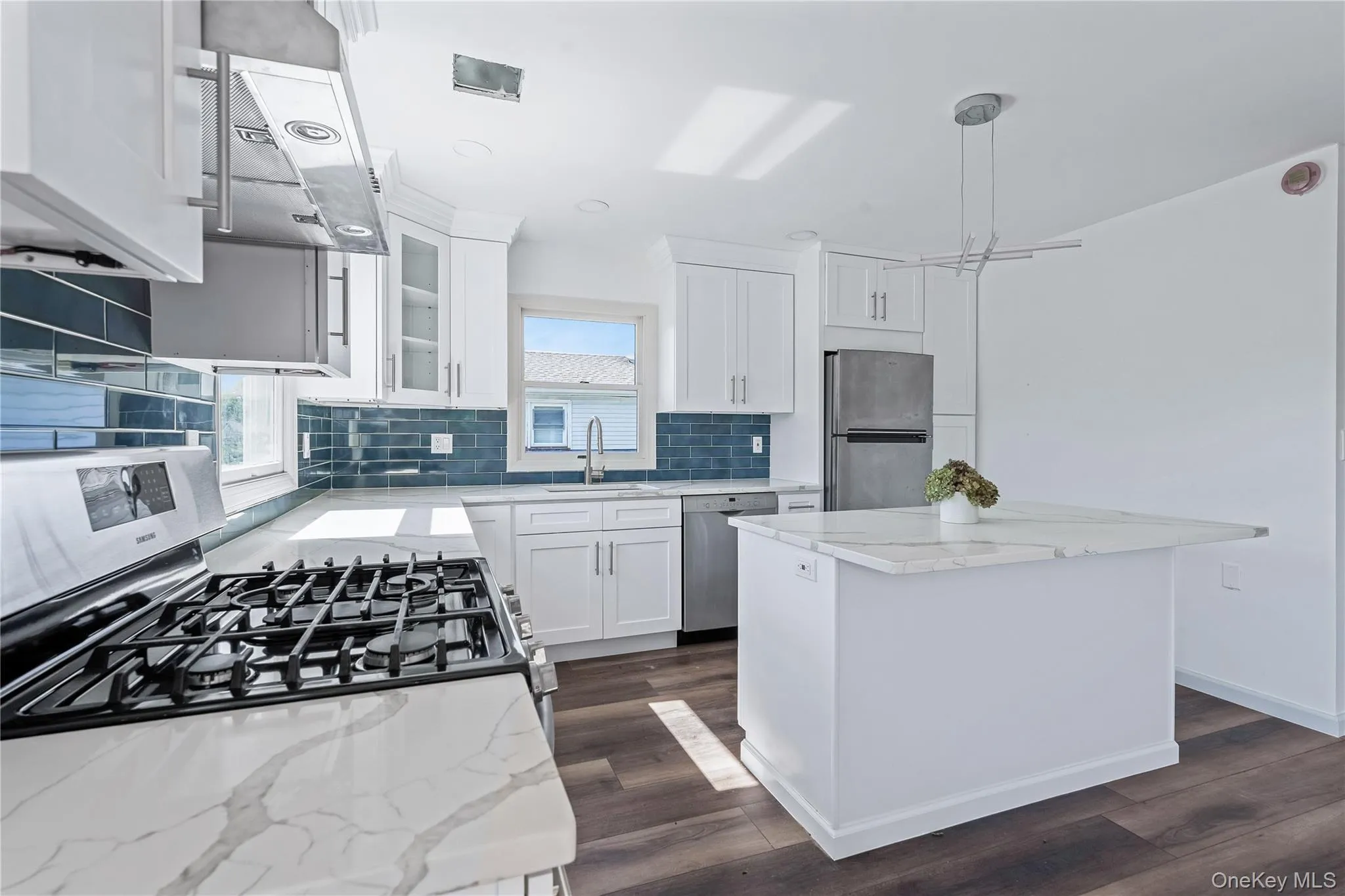 Kitchen with appliances with stainless steel finishes, tasteful backsplash, white cabinetry, a kitchen island, and light stone counters Kitchen with appliances with stainless steel finishes, tasteful backsplash, white cabinetry, a kitchen island, and light stone counters