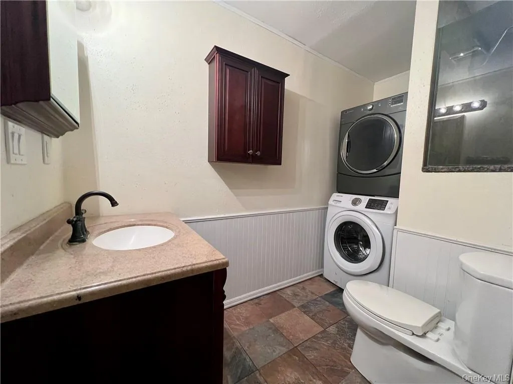 Full bathroom with vanity, wainscoting, stacked washer / dryer, and dark stone finish flooring Full bathroom with vanity, wainscoting, stacked washer / dryer, and dark stone finish flooring