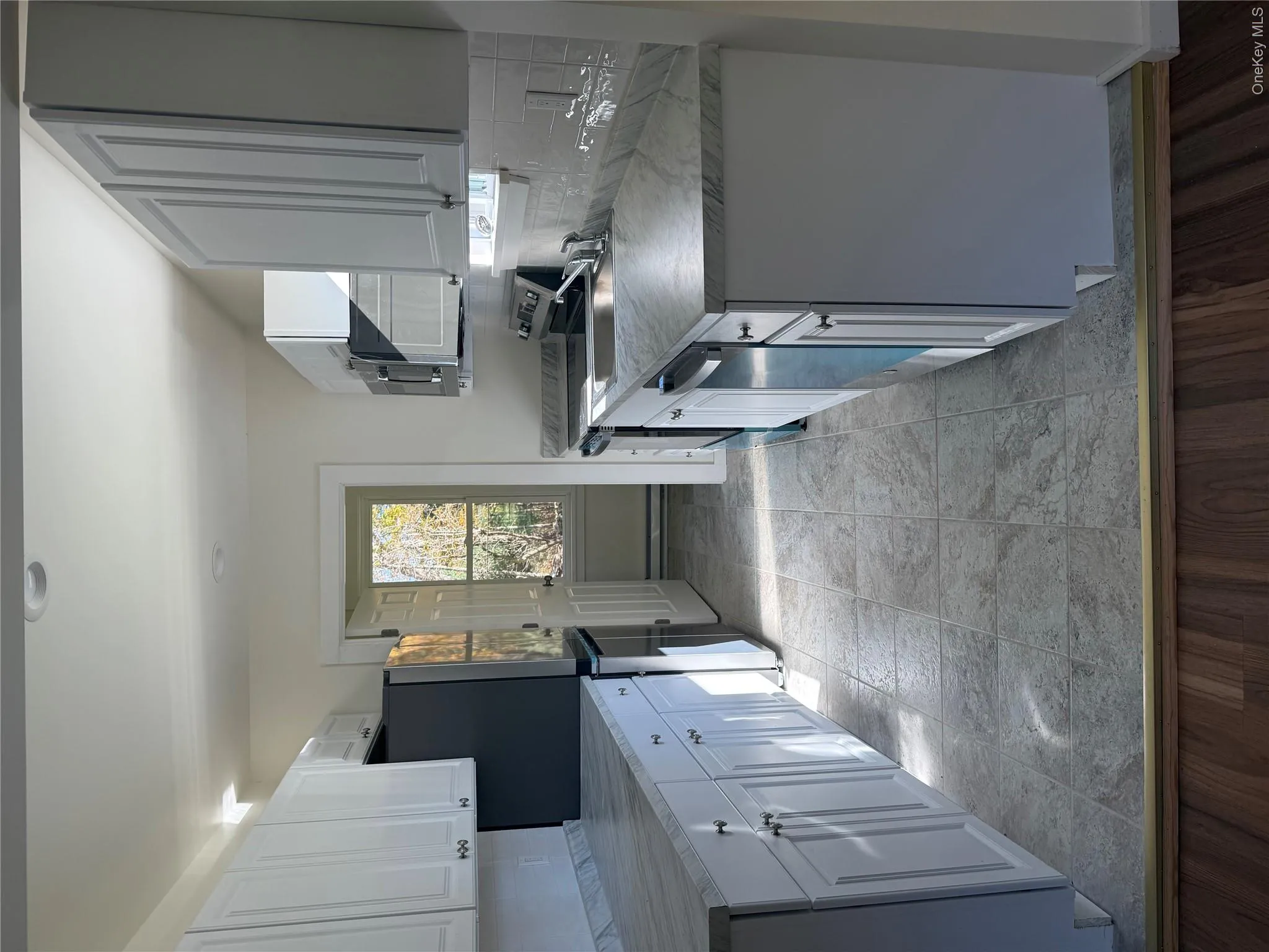 Kitchen with stainless steel appliances, light countertops, white cabinetry, baseboard heating, and light wood-style floors Kitchen with stainless steel appliances, light countertops, white cabinetry, baseboard heating, and light wood-style floors