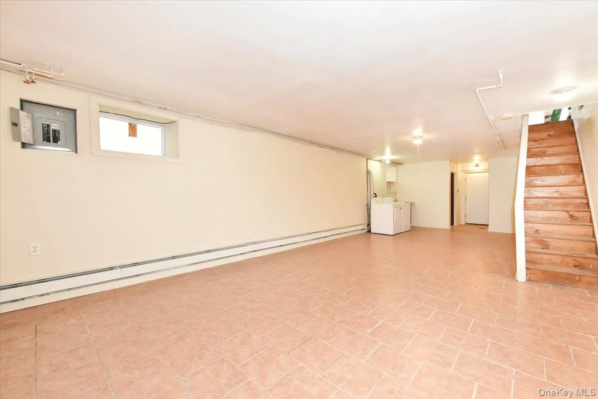 Basement featuring stairs, a baseboard radiator, and electric panel Basement featuring stairs, a baseboard radiator, and electric panel