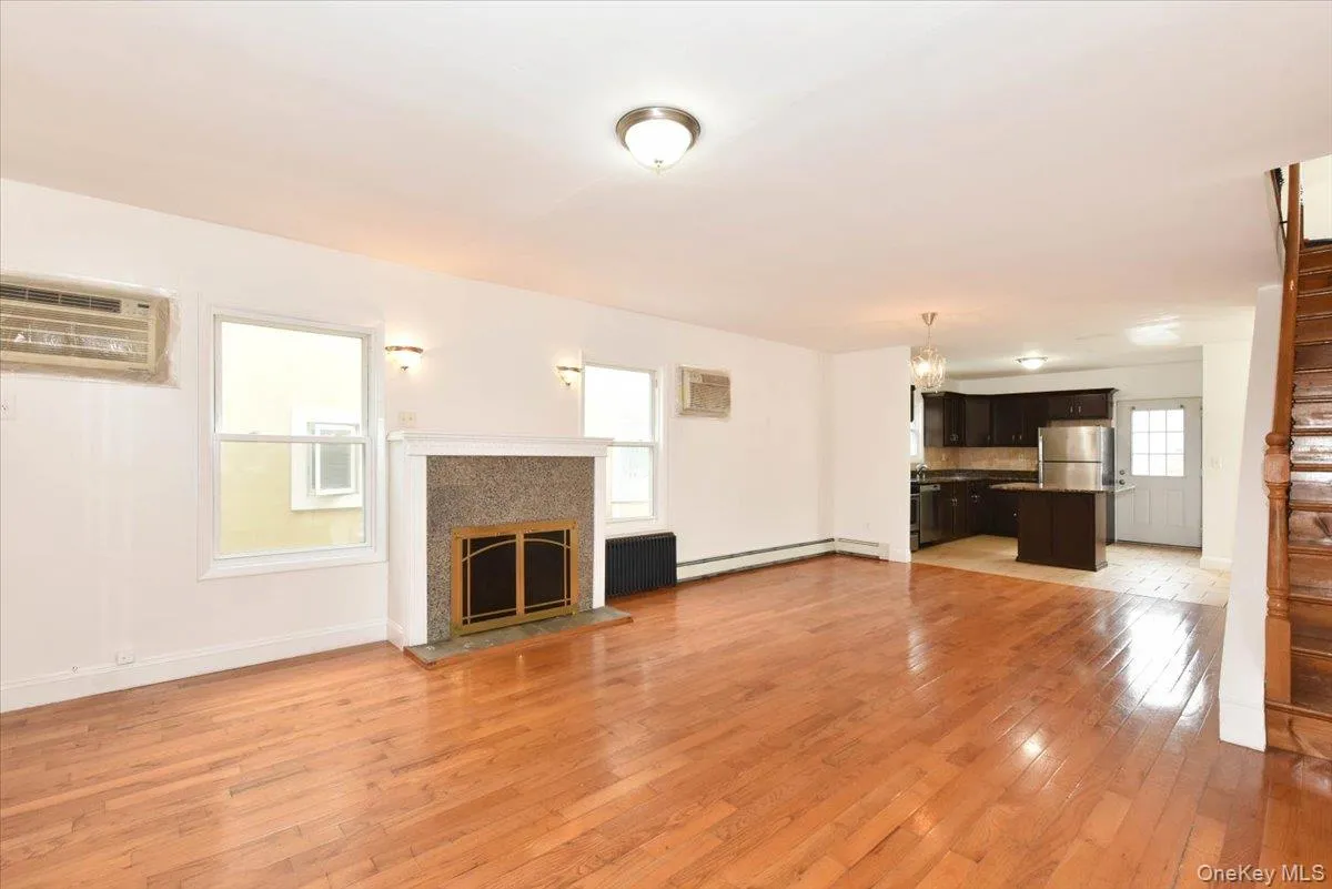 Unfurnished living room with light wood-style floors, a glass covered fireplace, radiator, a chandelier, and stairs Unfurnished living room with light wood-style floors, a glass covered fireplace, radiator, a chandelier, and stairs