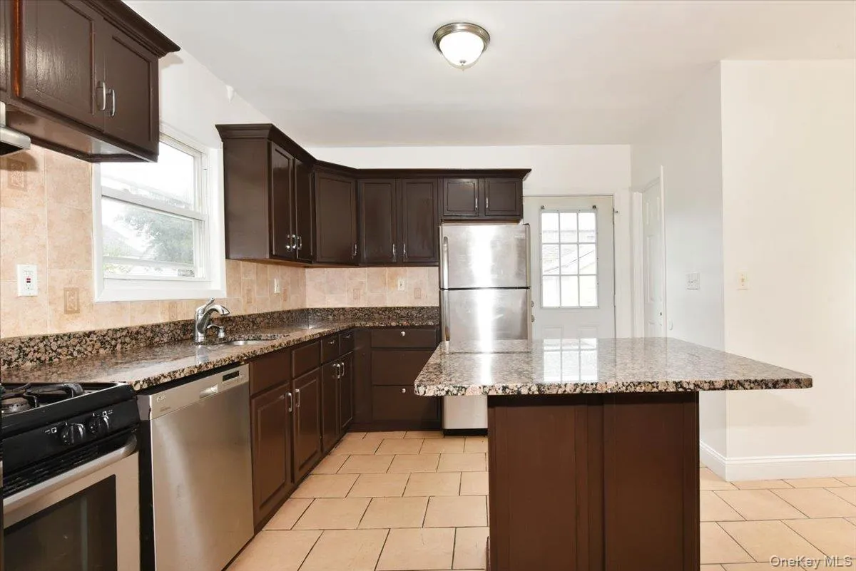 Kitchen featuring dark brown cabinetry, appliances with stainless steel finishes, dark stone countertops, and a kitchen island Kitchen featuring dark brown cabinetry, appliances with stainless steel finishes, dark stone countertops, and a kitchen island
