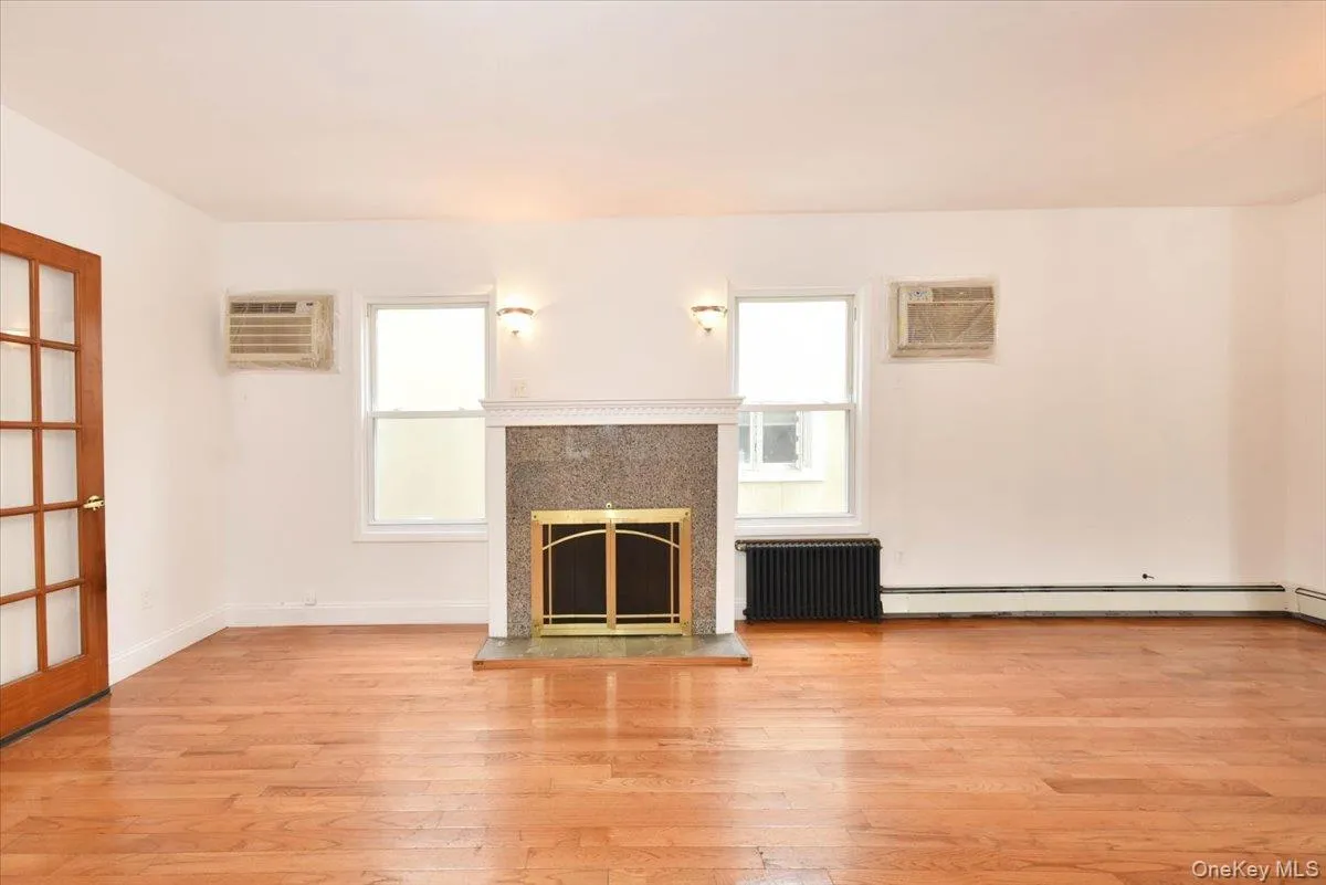 Unfurnished living room featuring radiator heating unit, wood finished floors, a fireplace, and a wall mounted AC Unfurnished living room featuring radiator heating unit, wood finished floors, a fireplace, and a wall mounted AC