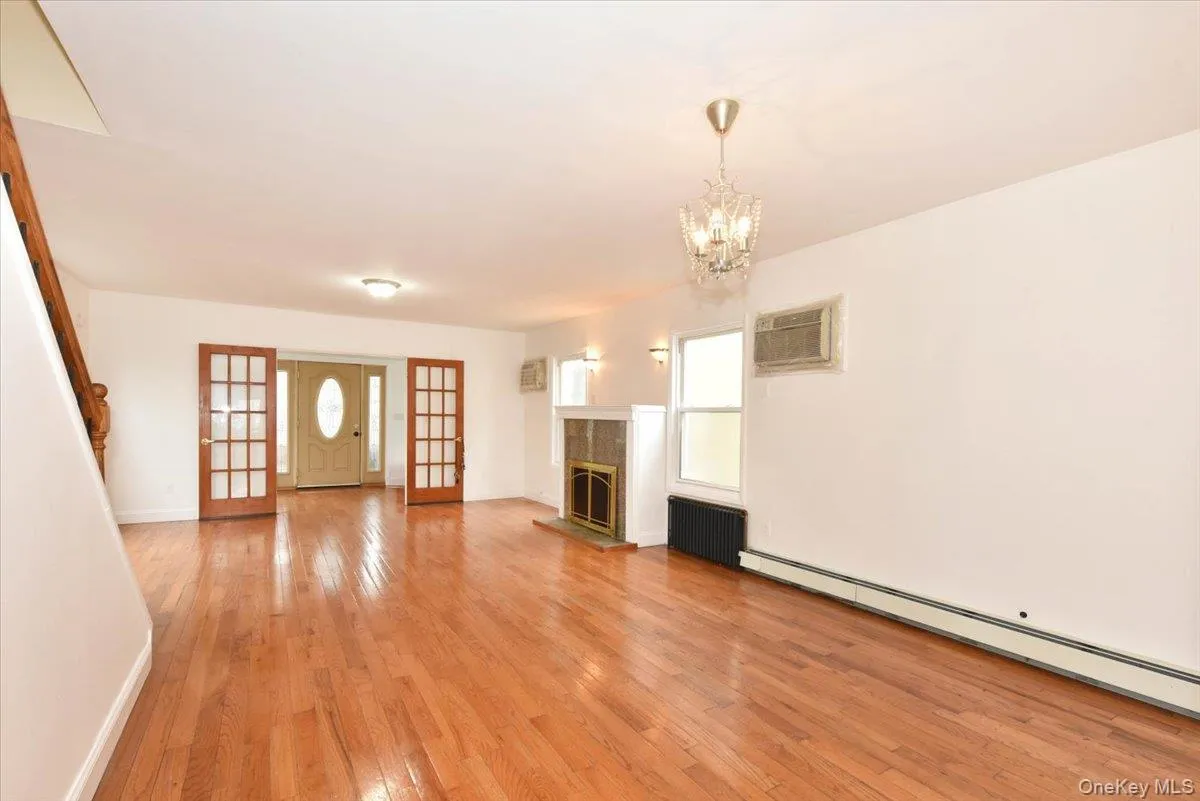 Unfurnished living room featuring light wood-style floors, a baseboard radiator, a tiled fireplace, radiator, and a chandelier Unfurnished living room featuring light wood-style floors, a baseboard radiator, a tiled fireplace, radiator, and a chandelier