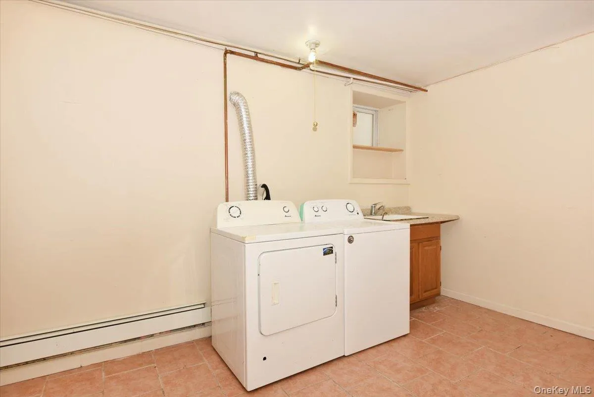 Washroom with a baseboard radiator, light tile patterned floors, and separate washer and dryer Washroom with a baseboard radiator, light tile patterned floors, and separate washer and dryer