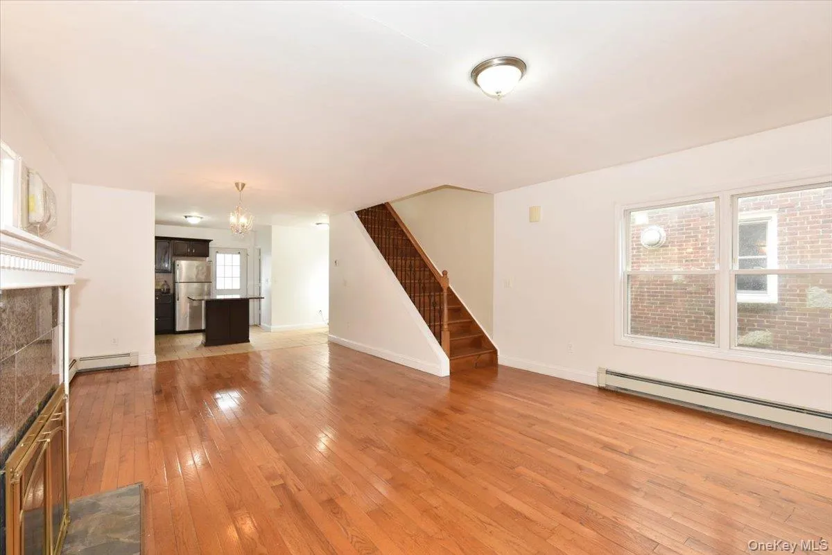 Unfurnished living room featuring light wood-style flooring, a fireplace, stairway, a chandelier, and a baseboard radiator Unfurnished living room featuring light wood-style flooring, a fireplace, stairway, a chandelier, and a baseboard radiator