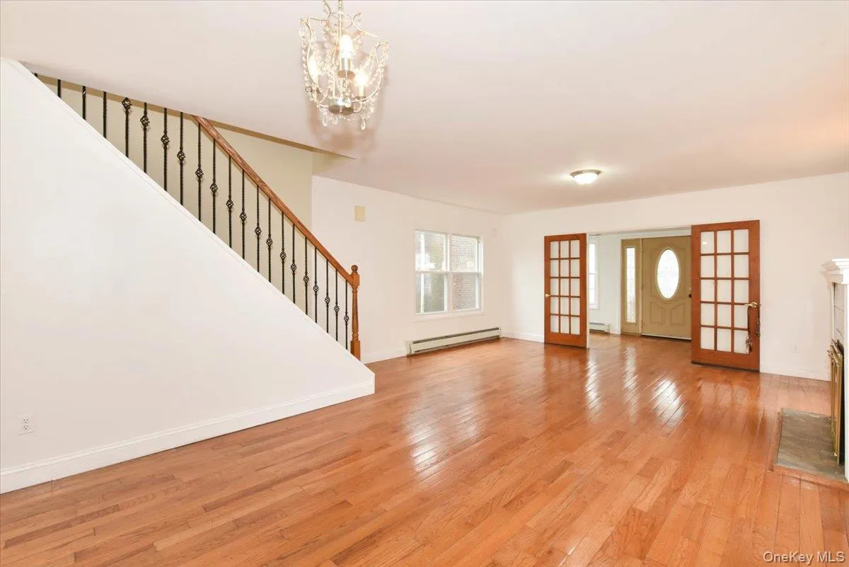 Unfurnished living room featuring light wood-style floors, stairs, a baseboard heating unit, a chandelier, and french doors Unfurnished living room featuring light wood-style floors, stairs, a baseboard heating unit, a chandelier, and french doors