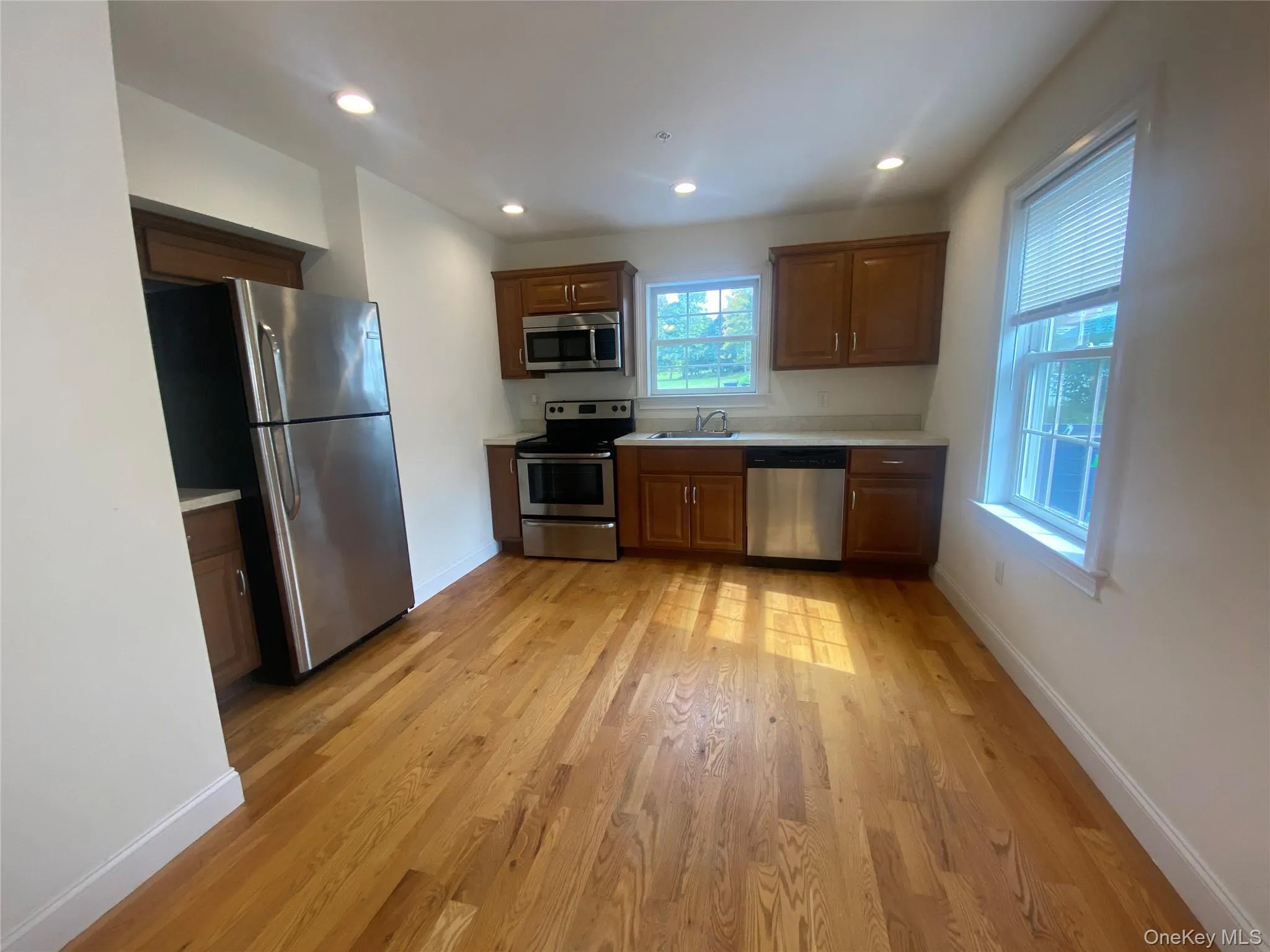 Kitchen featuring light countertops, appliances with stainless steel finishes, light wood-style floors, recessed lighting, and brown cabinetry Kitchen featuring light countertops, appliances with stainless steel finishes, light wood-style floors, recessed lighting, and brown cabinetry