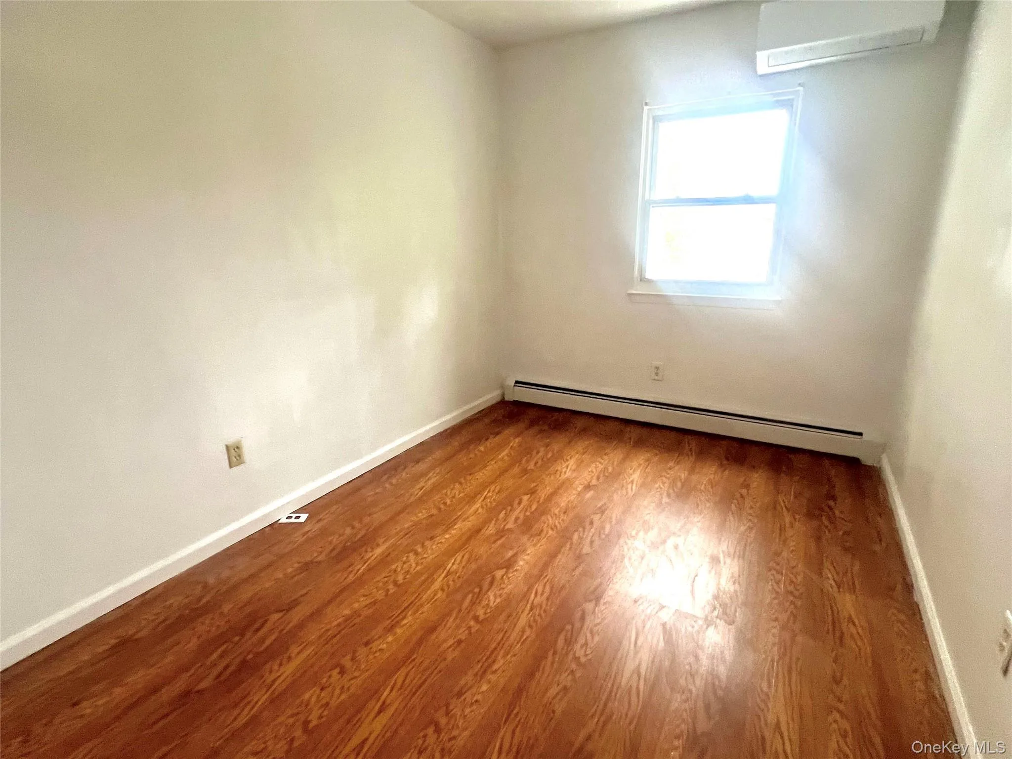 Spare room featuring a baseboard radiator, a wall unit AC, and wood finished floors Spare room featuring a baseboard radiator, a wall unit AC, and wood finished floors