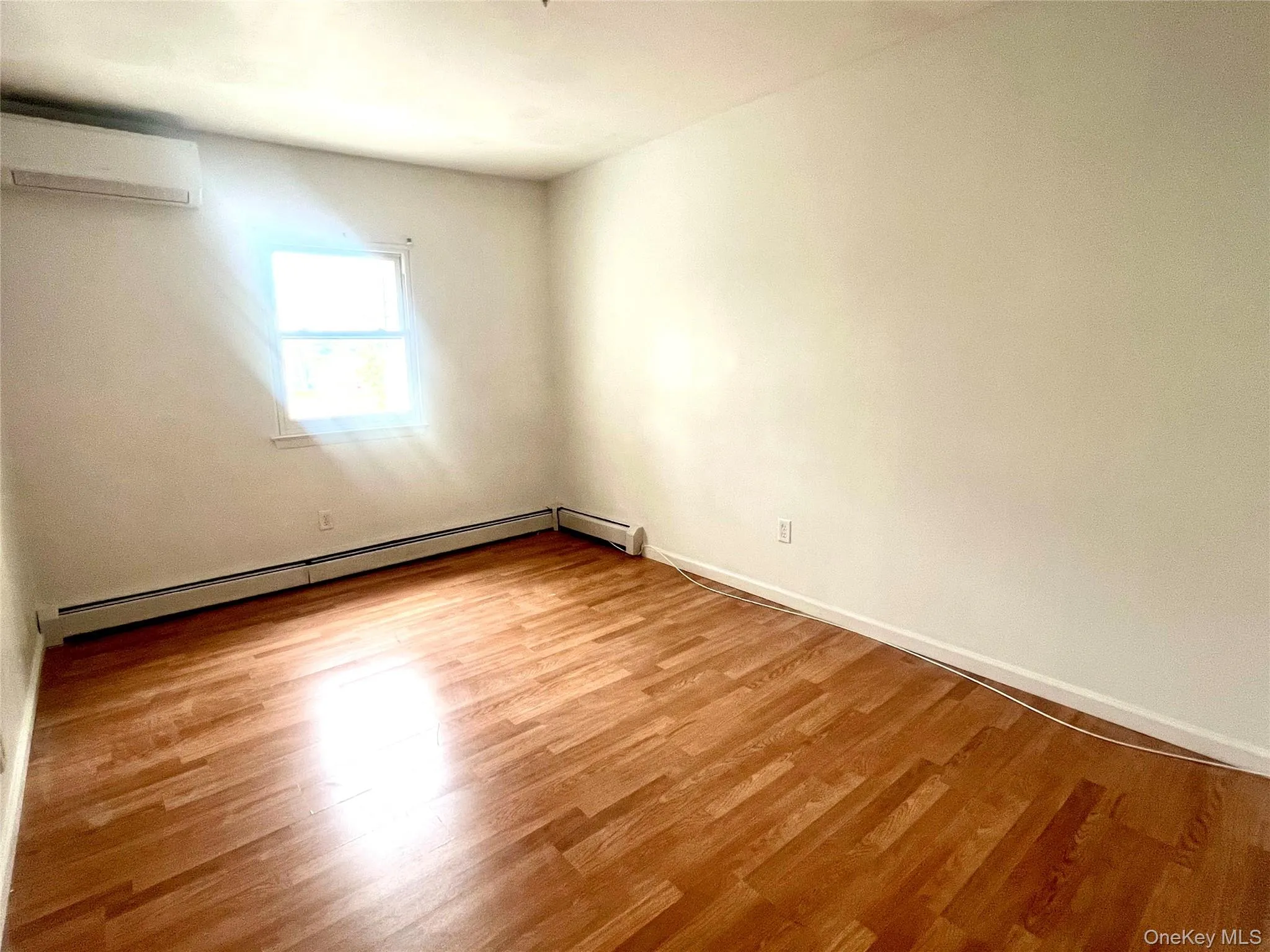 Spare room with light wood-style flooring, an AC wall unit, and a baseboard heating unit Spare room with light wood-style flooring, an AC wall unit, and a baseboard heating unit